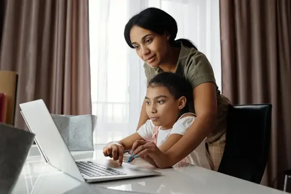 Mother guiding her child while using a laptop