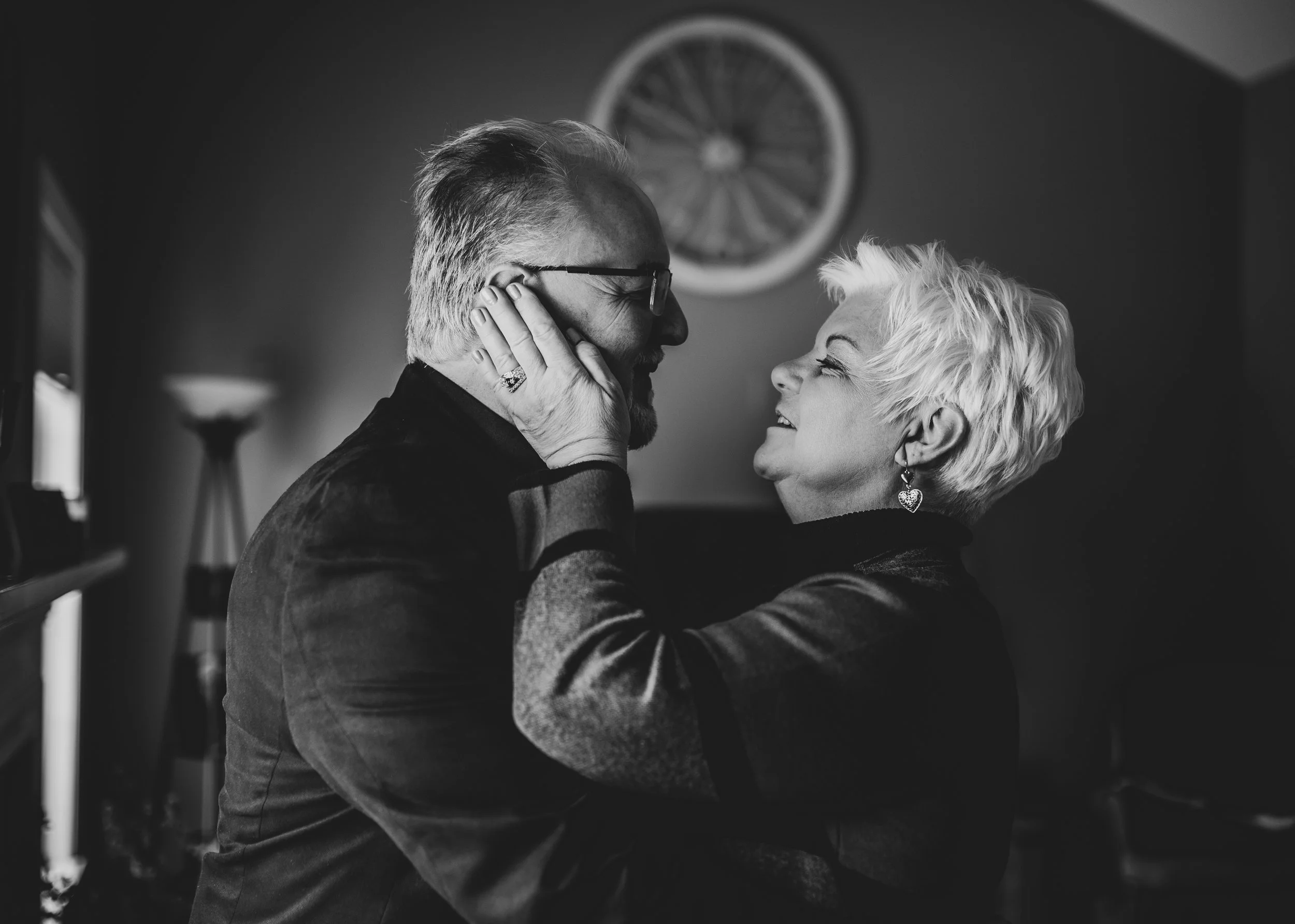 A black and white photo of an older couple smiling and gazing into each other's eyes, with the woman touching the man's face gently.
