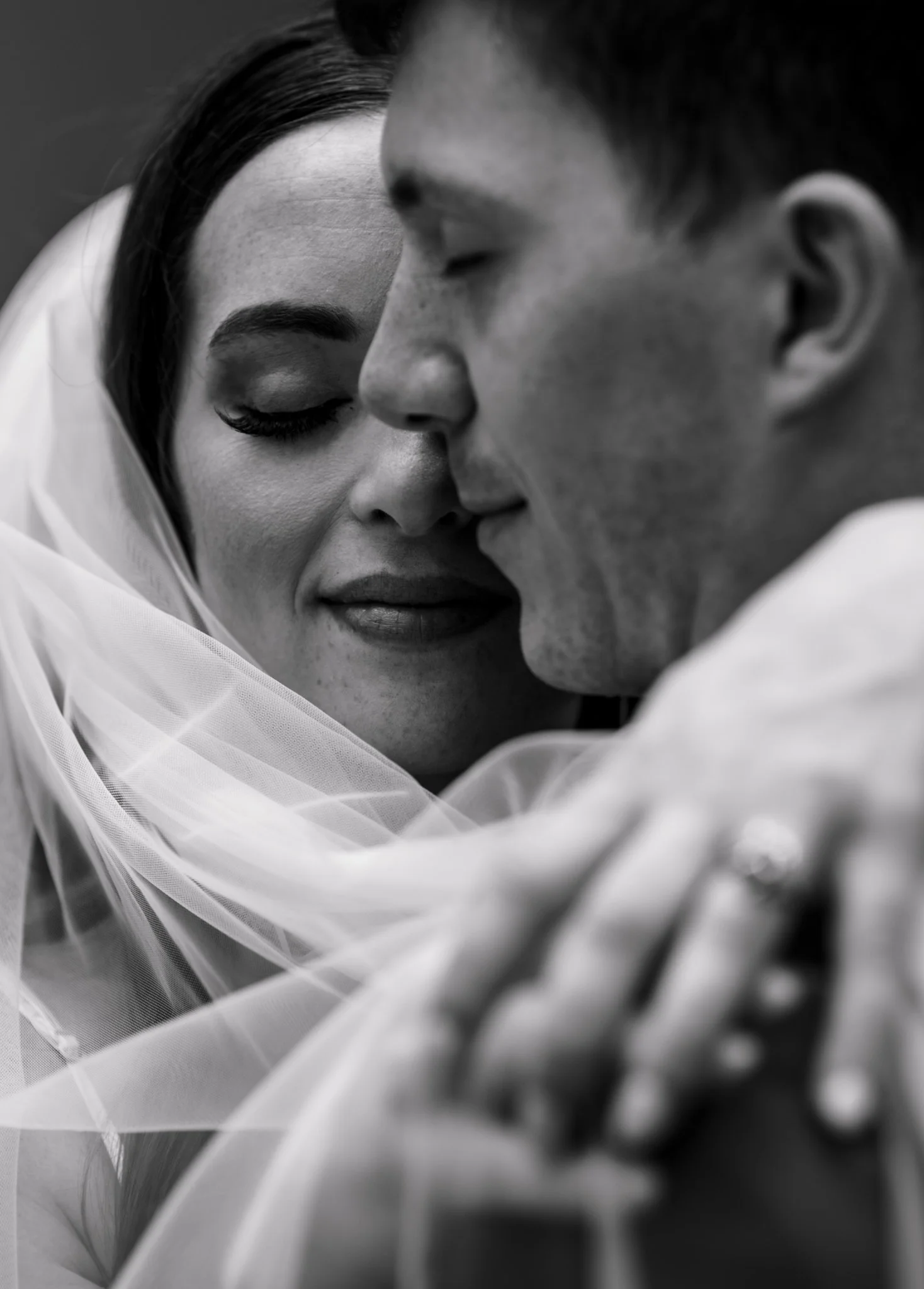 A close-up black and white photo of a couple in an intimate embrace, with their faces close together and eyes closed.