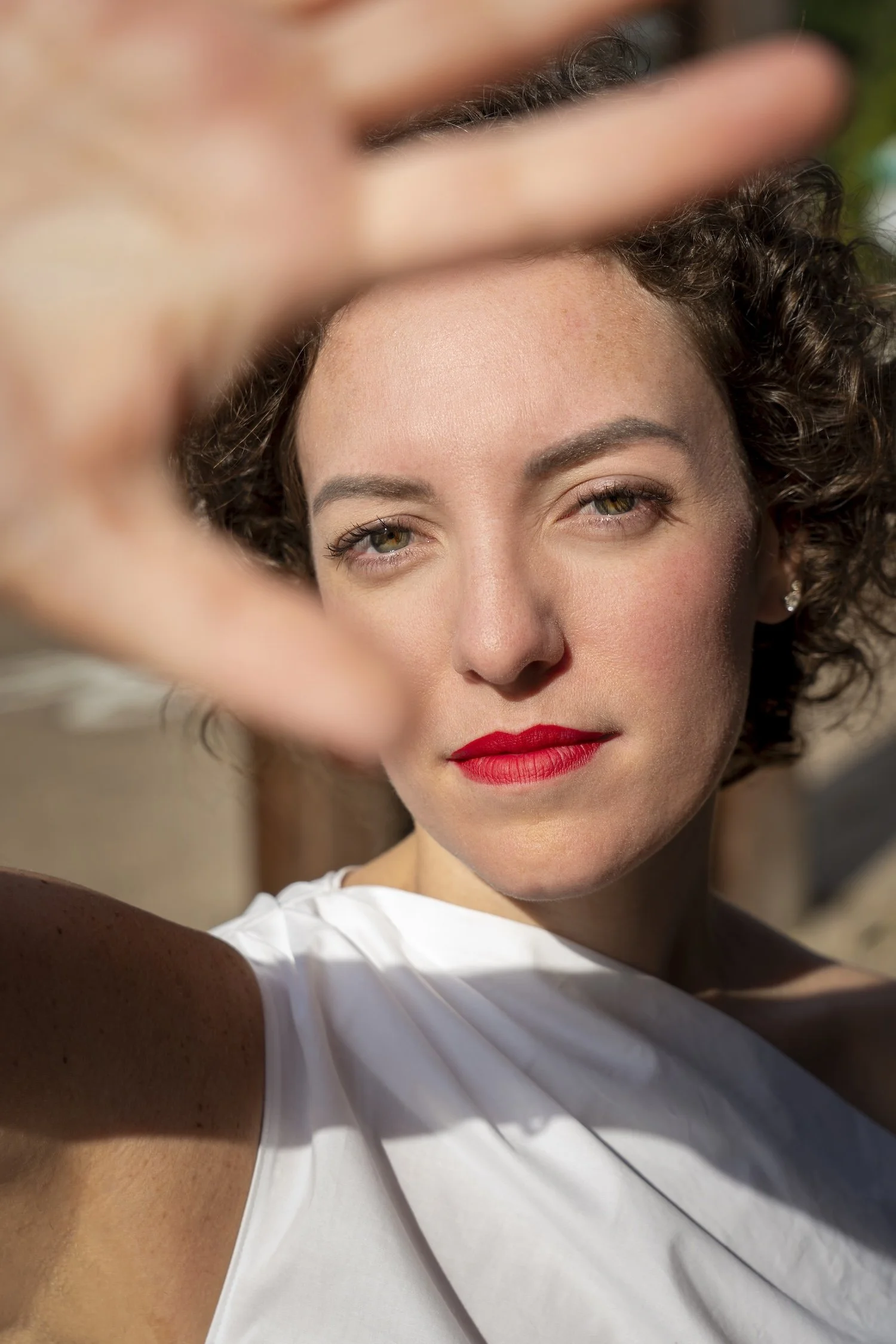 Copywriter and Bigmouth Copy CEO, Taylor de la Fuente, holds her hand up to the sun and she smiles gently at the camera. She's wearing red lipstick and a white blouse.