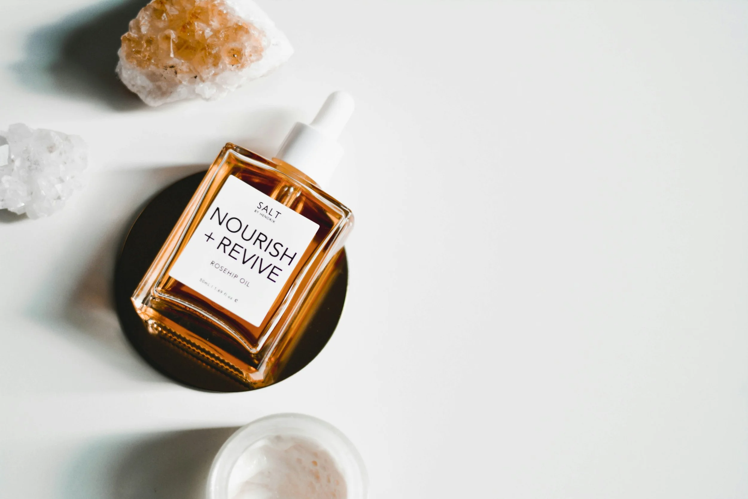 A square bottle of rosehip oil surrounded by crystals on a white surface table.