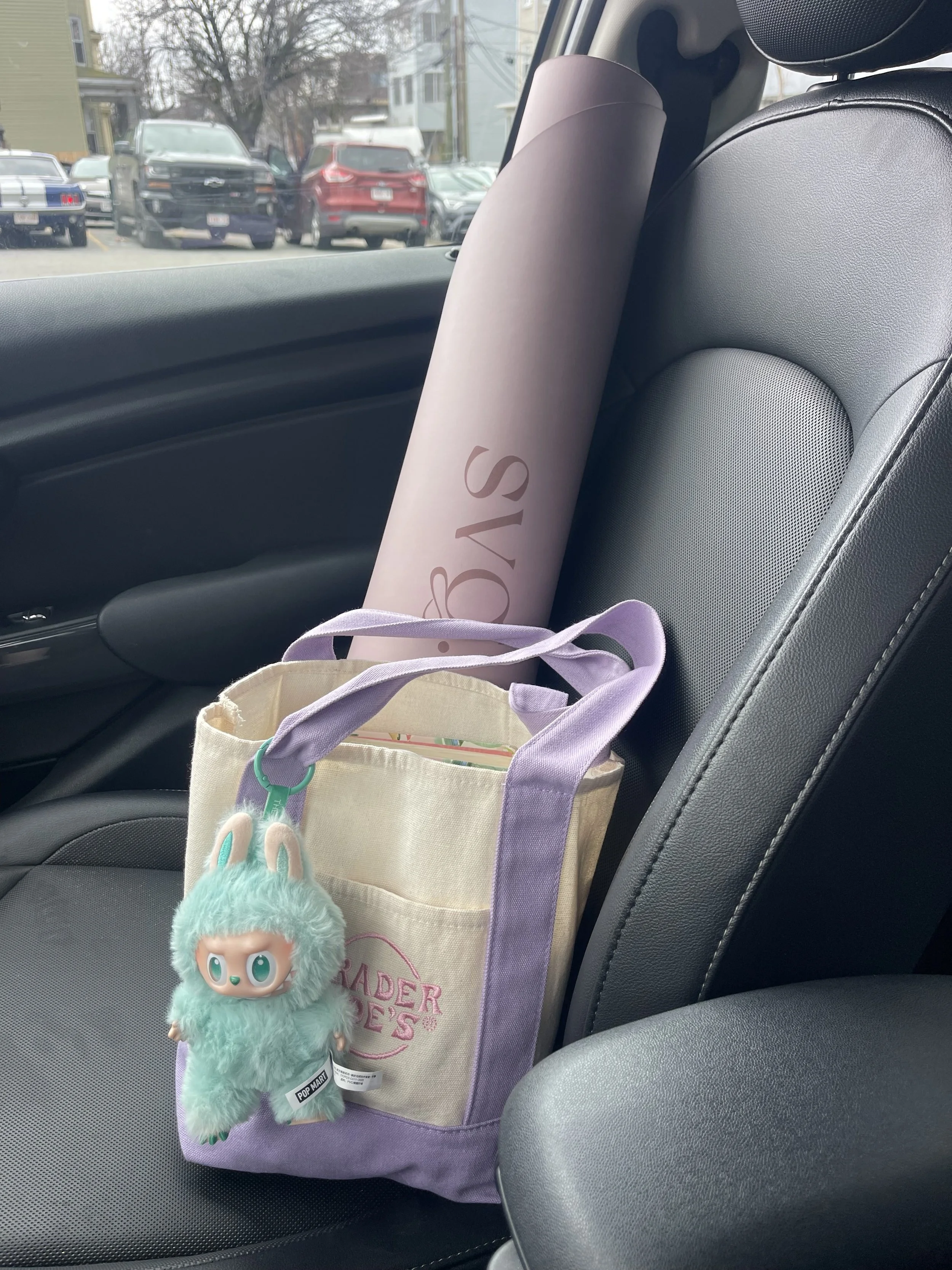 The lila serena capsula mat rolled up and placed in the passenger seat of the car with a canvas tote and labubu.