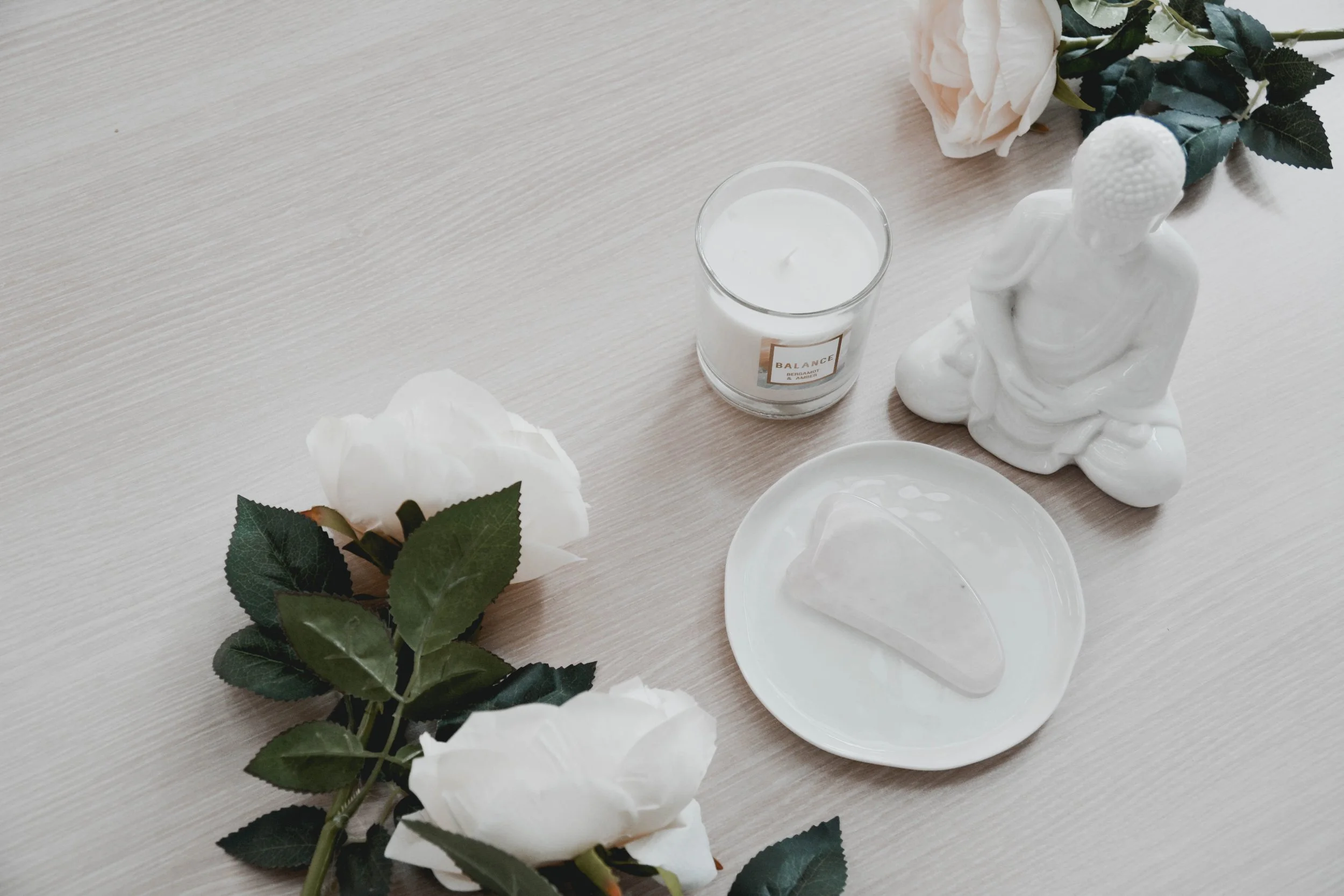 White Ceramic Plate with White Roses Beside a Candle and Buddha Figure