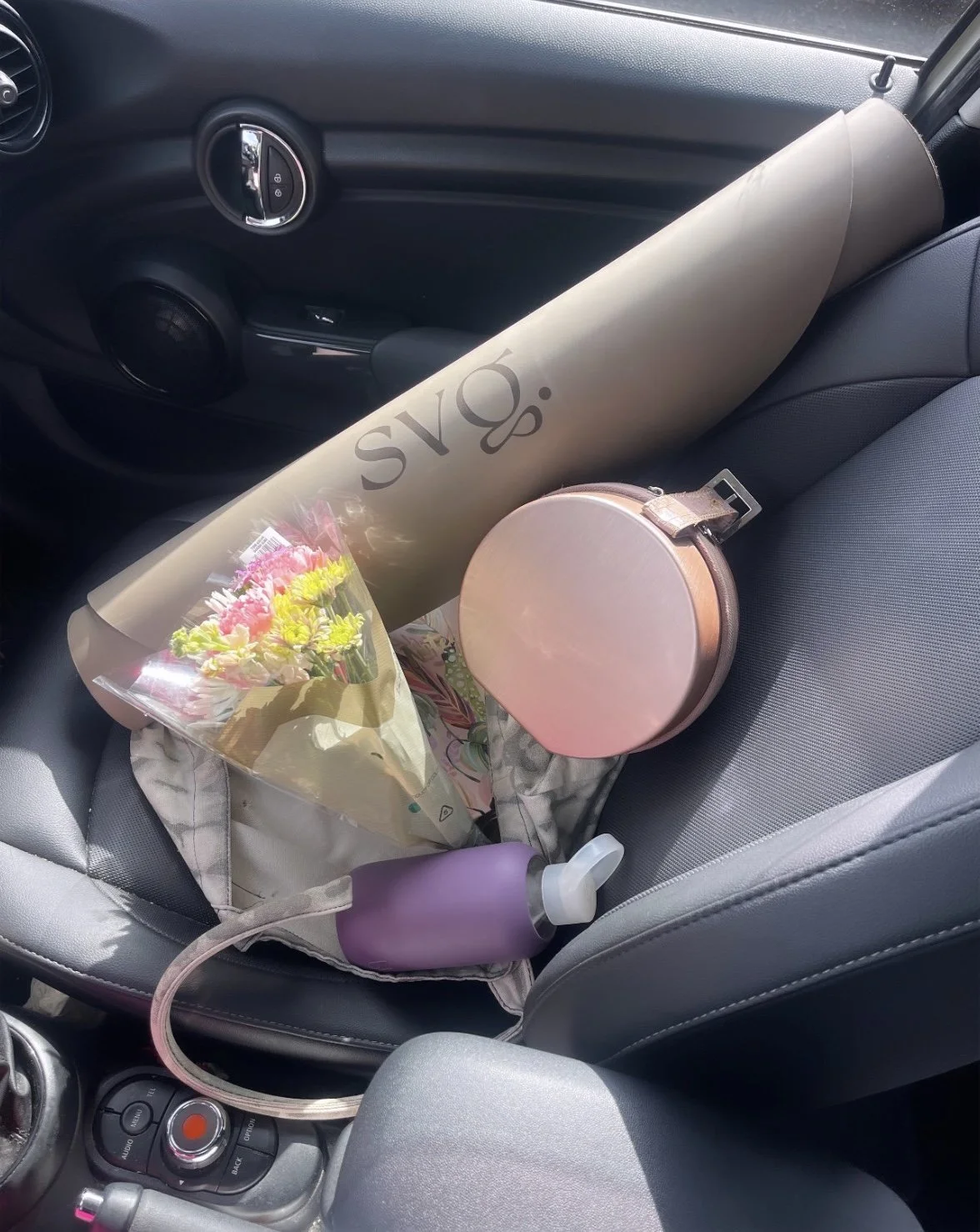 the perla de leche capsula mat rolled up in the passenger seat of a car with a bouquet of flowers, water bottle, and handbag.