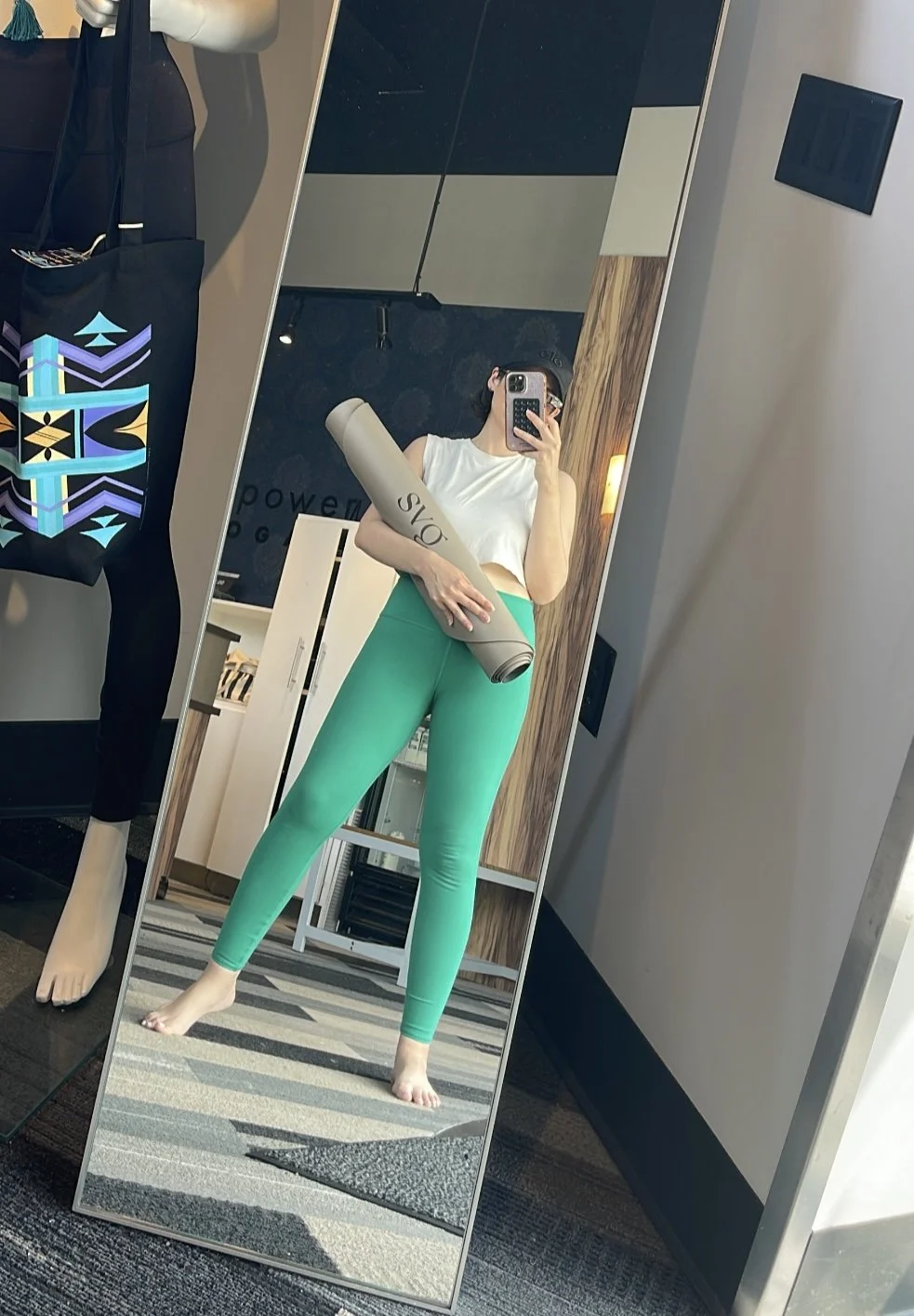 a woman taking a picture of herself in the mirror with her perla de leche capsula mat rolled up in her arm.