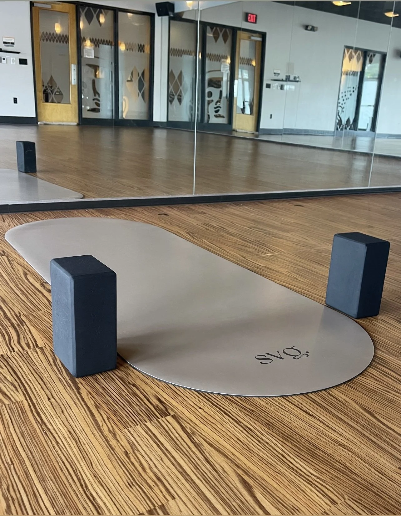 the perla de leche capsula mat laid out on the hardwood floor with yoga blocks in a yoga studio.