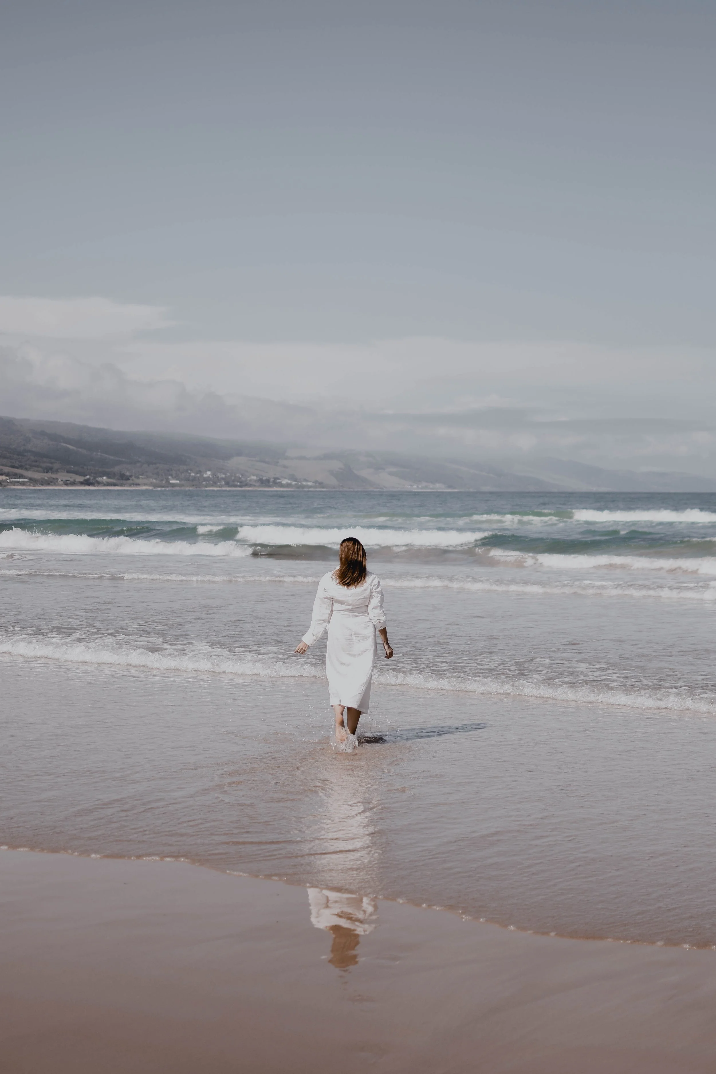 A woman dressed in white walking on the beach