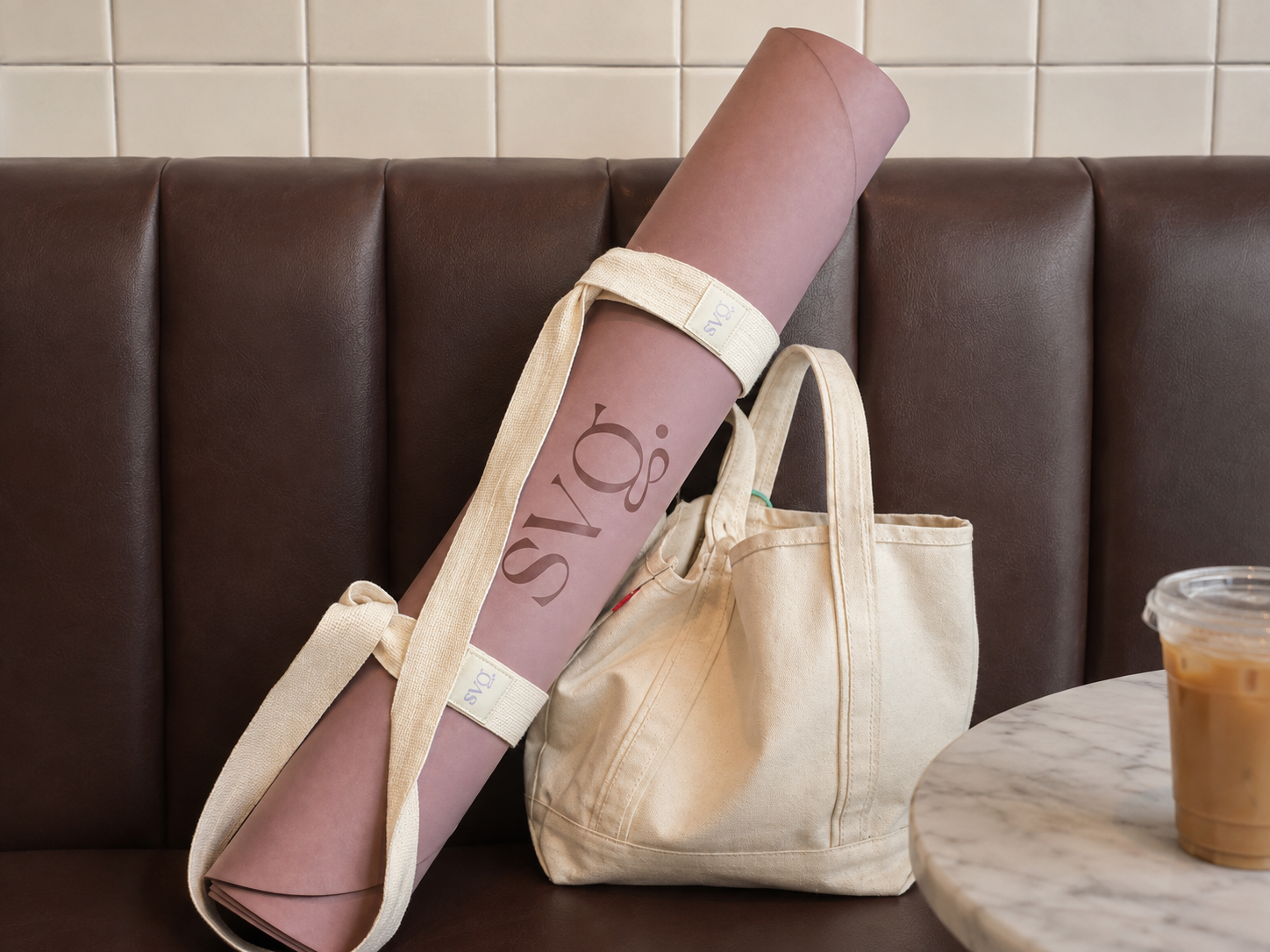 The Lila Serena Capsula Mat rolled up tightly in the Ritual Mat Strap on leather seats with a neutral tote at a coffee shop.