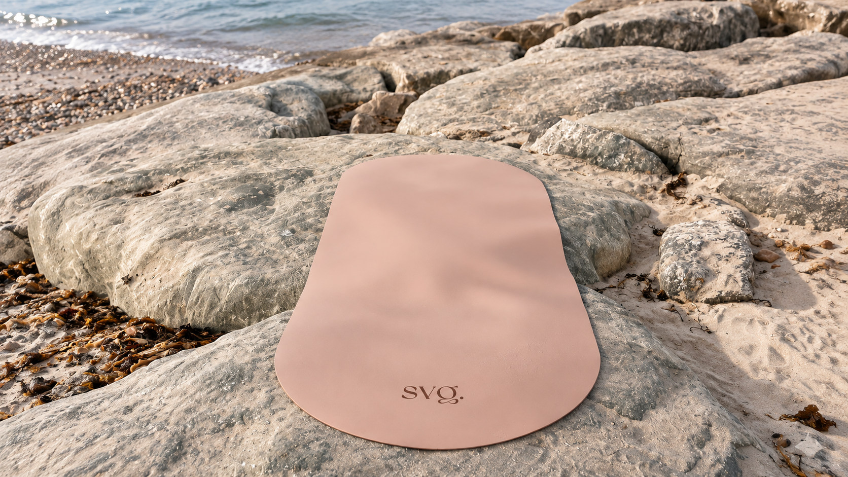 The Arena Sol Capsula Wellness Mat laid out over rocks at the beach.