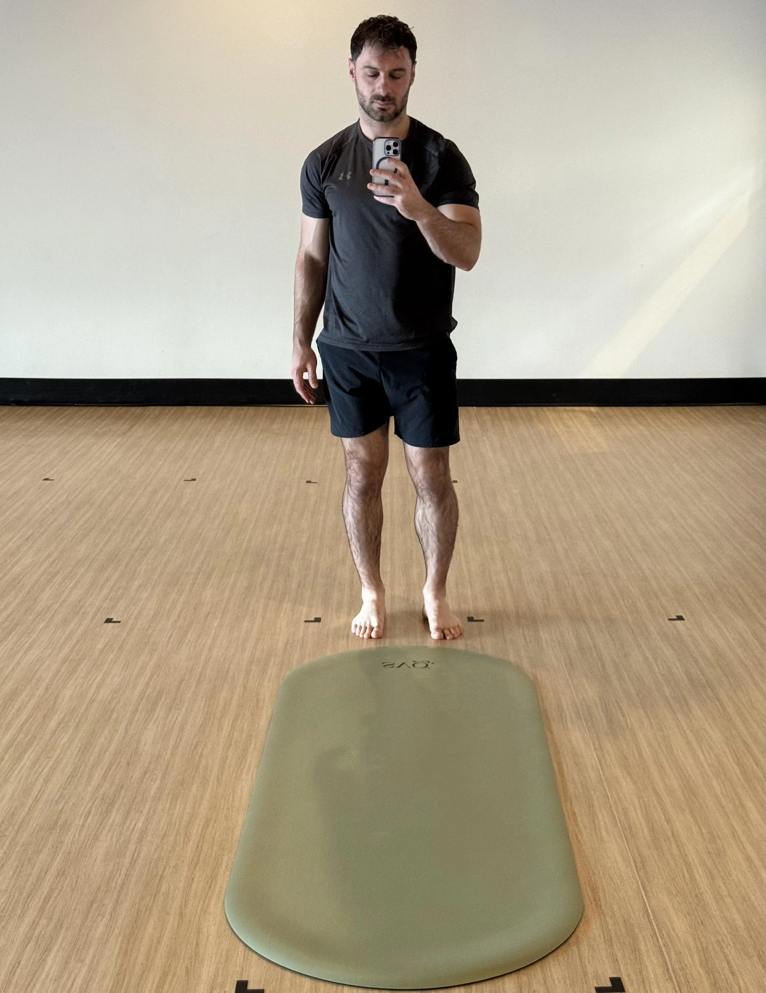 a man taking a picture of himself in the mirror with the oliva verde capsula mat laid out in a studio.