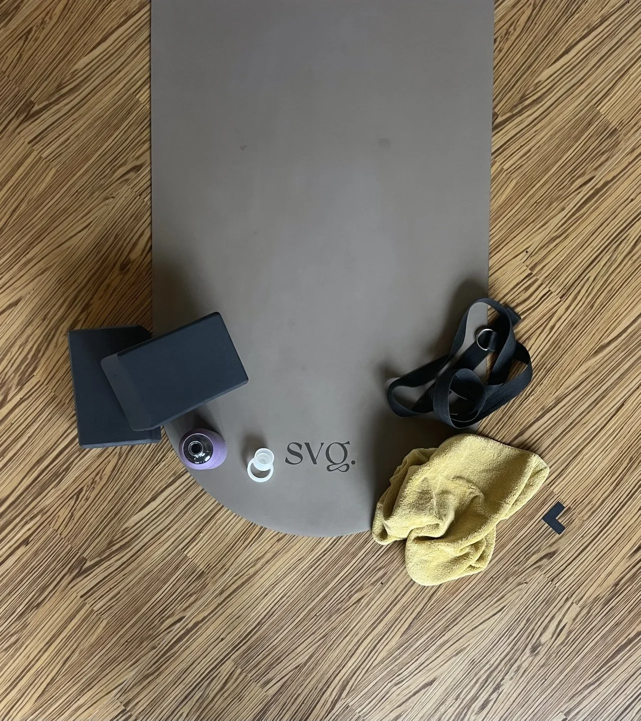 perla de leche capsula mat rolled out on the hardwood floor with yoga equipment, towel, and water bottle.