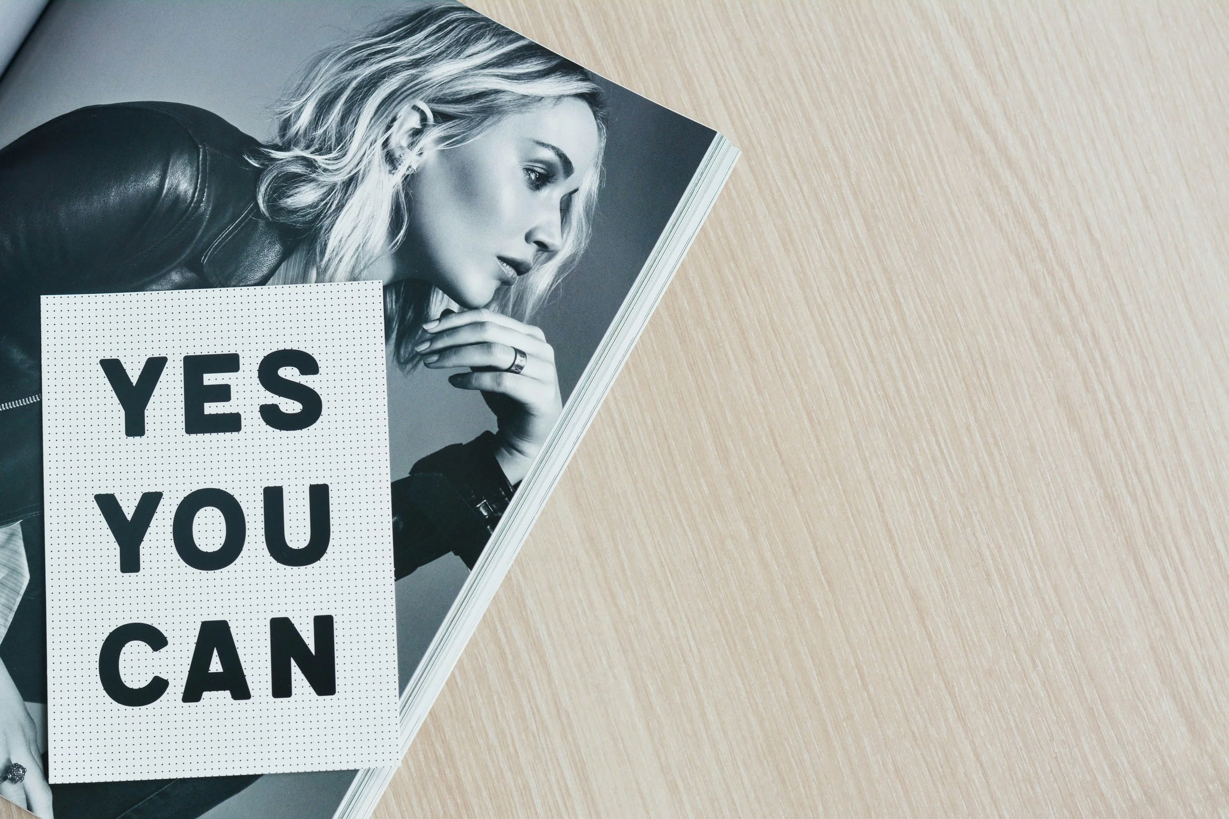 Yes You Can Magazine Cover in black and white on a wooden table surface.