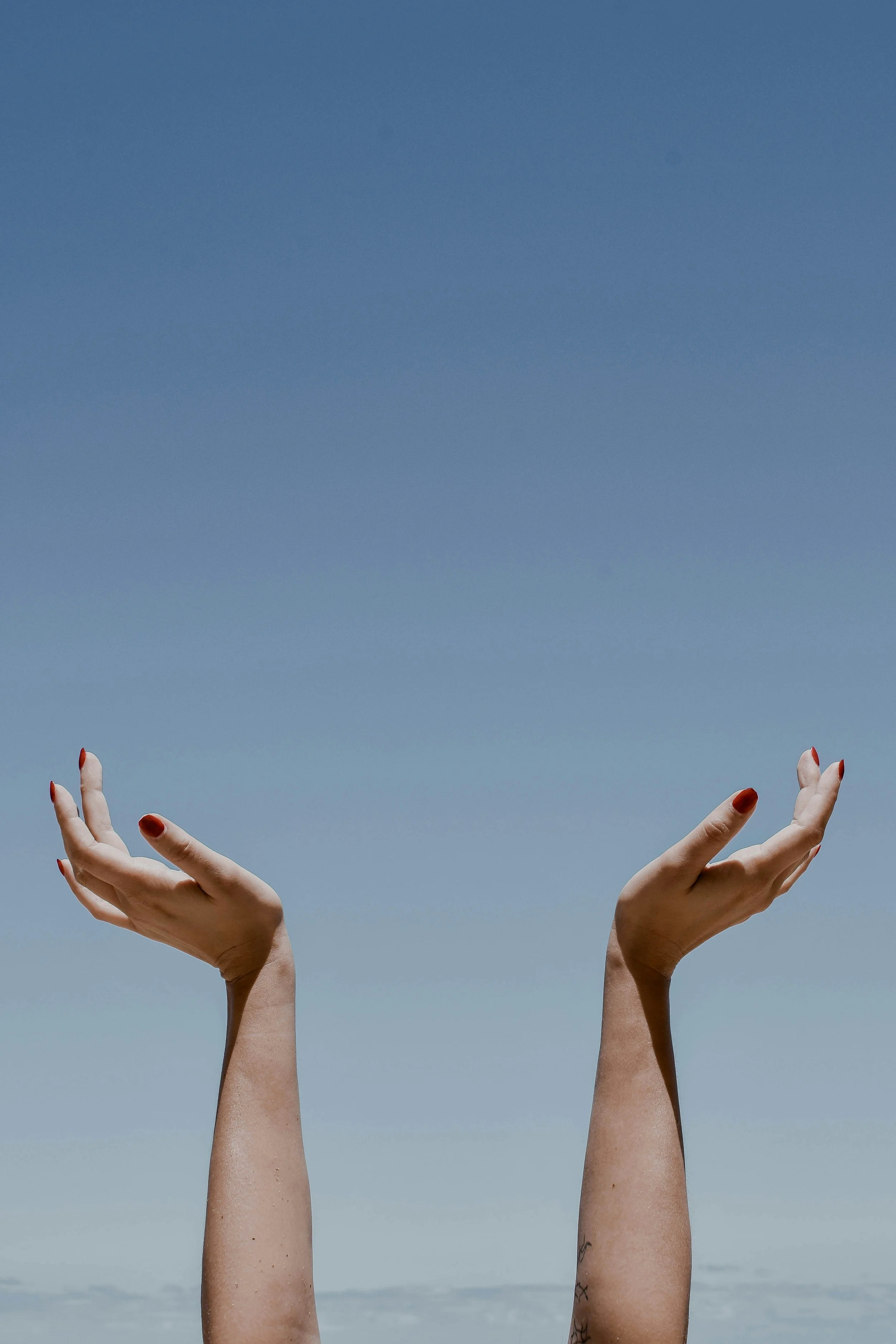 A woman's hands and arms are stretched towards a blue sky above