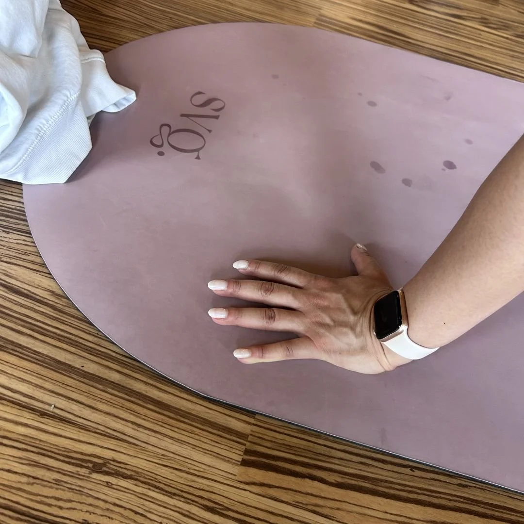 A shot of the lila serena capsula wellness mat with a focus on the top of the mat and "svg." logo with a woman's hand on the mat during practice.