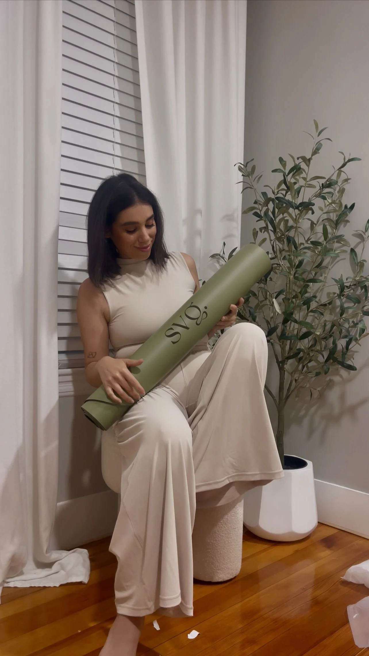 A woman seated on a stool and holding her oliva verde capsula mat in her hands.