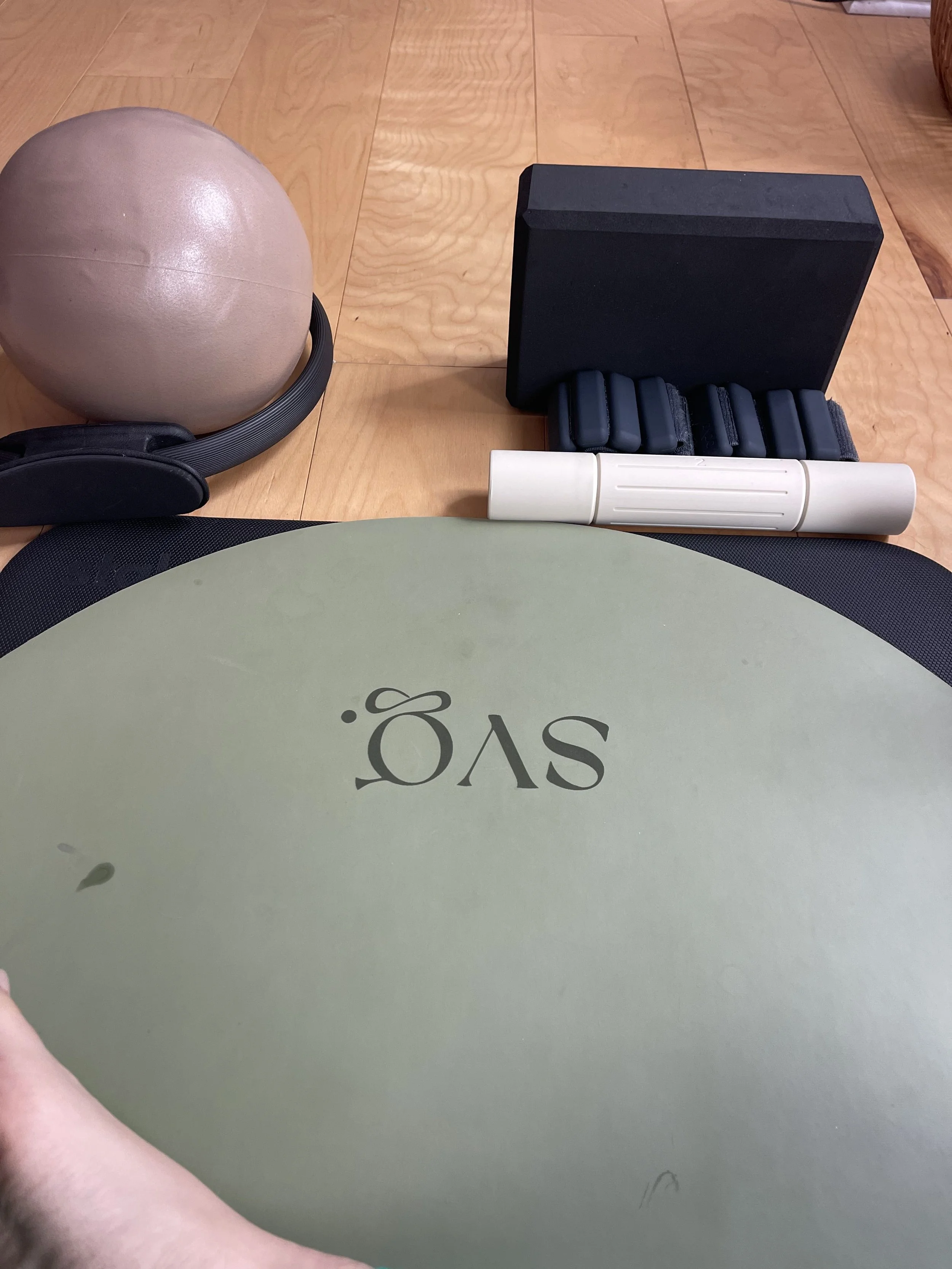 the oliva verde capsula mat laid out on the hardwood floor with pilates equipment.