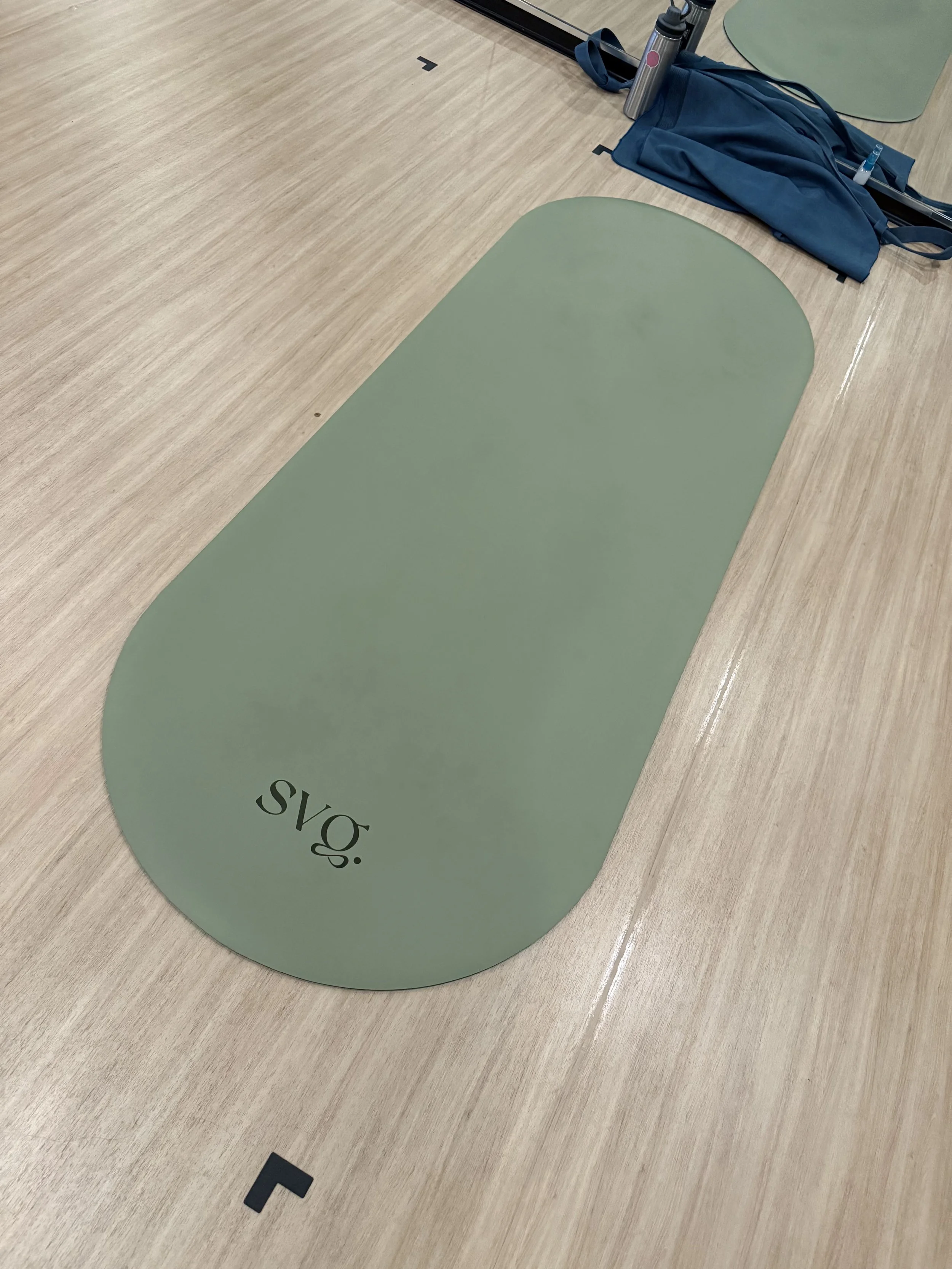 the oliva verde capsula mat laid out on the hardwood floor in a studio with yoga straps and towel.