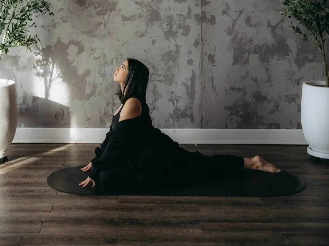A woman dressed in black doing a grounded yoga pose on the negro mate capsula mat with a soft beautiful interior back drop.