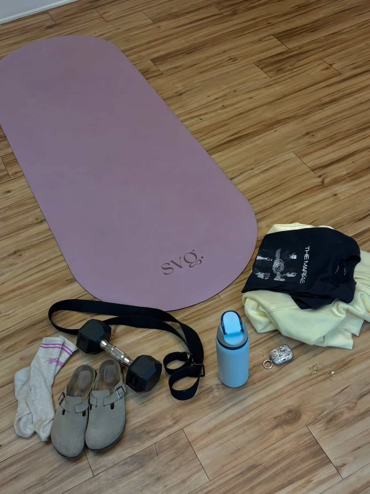 The lila serena capsula mat is rolled out on the hardwood floor with fitness equipment.