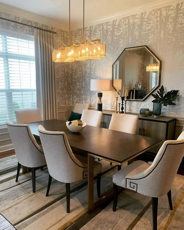 Modern dining room featuring a dark wooden table, six upholstered chairs, a geometric chandelier, and a large decorative mirror. The room is decorated with a sideboard, vases, and curtains on the window.