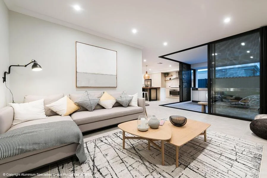 Modern living room with a beige sectional sofa, assorted pillows, abstract wall art, coffee table, and open-plan kitchen; large sliding glass doors open to a patio.