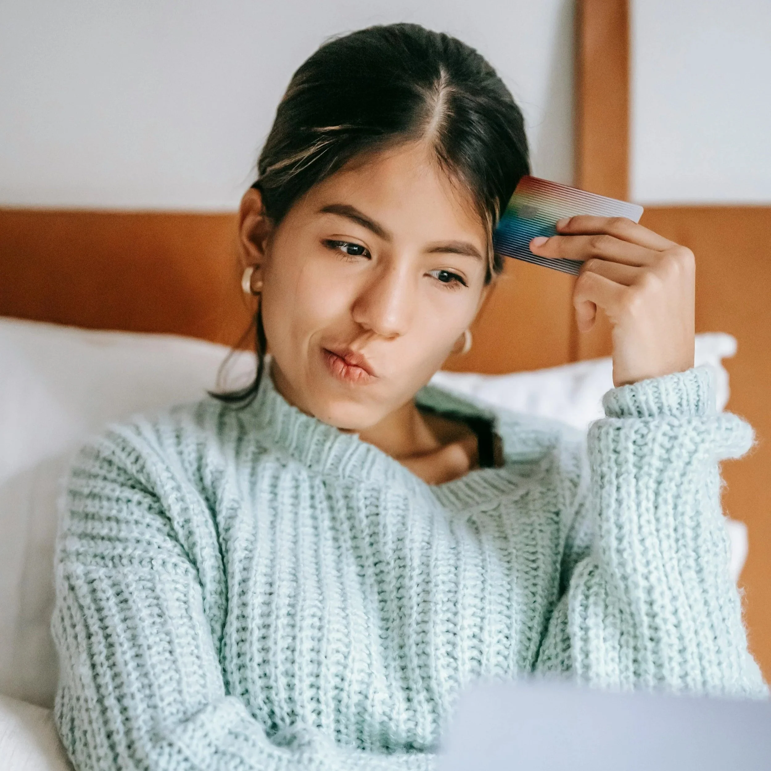 A woman sitting on a bed holding a credit card and laptop, reflecting thoughtful decision making, self awareness, and financial alignment.