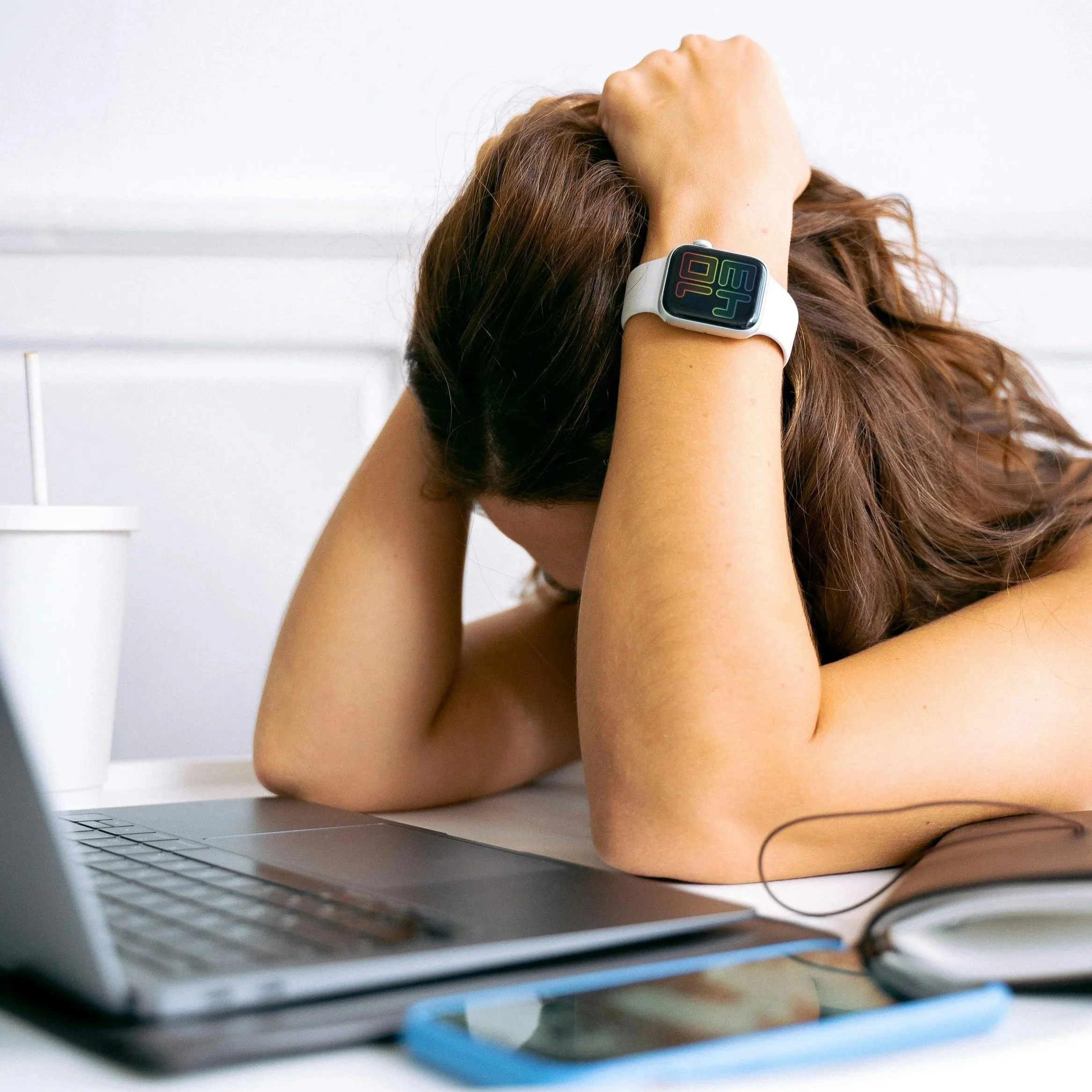 A woman sitting at a desk with her head resting in her hands while looking at a laptop, representing burnout, mental overwhelm, and misalignment in work and success.