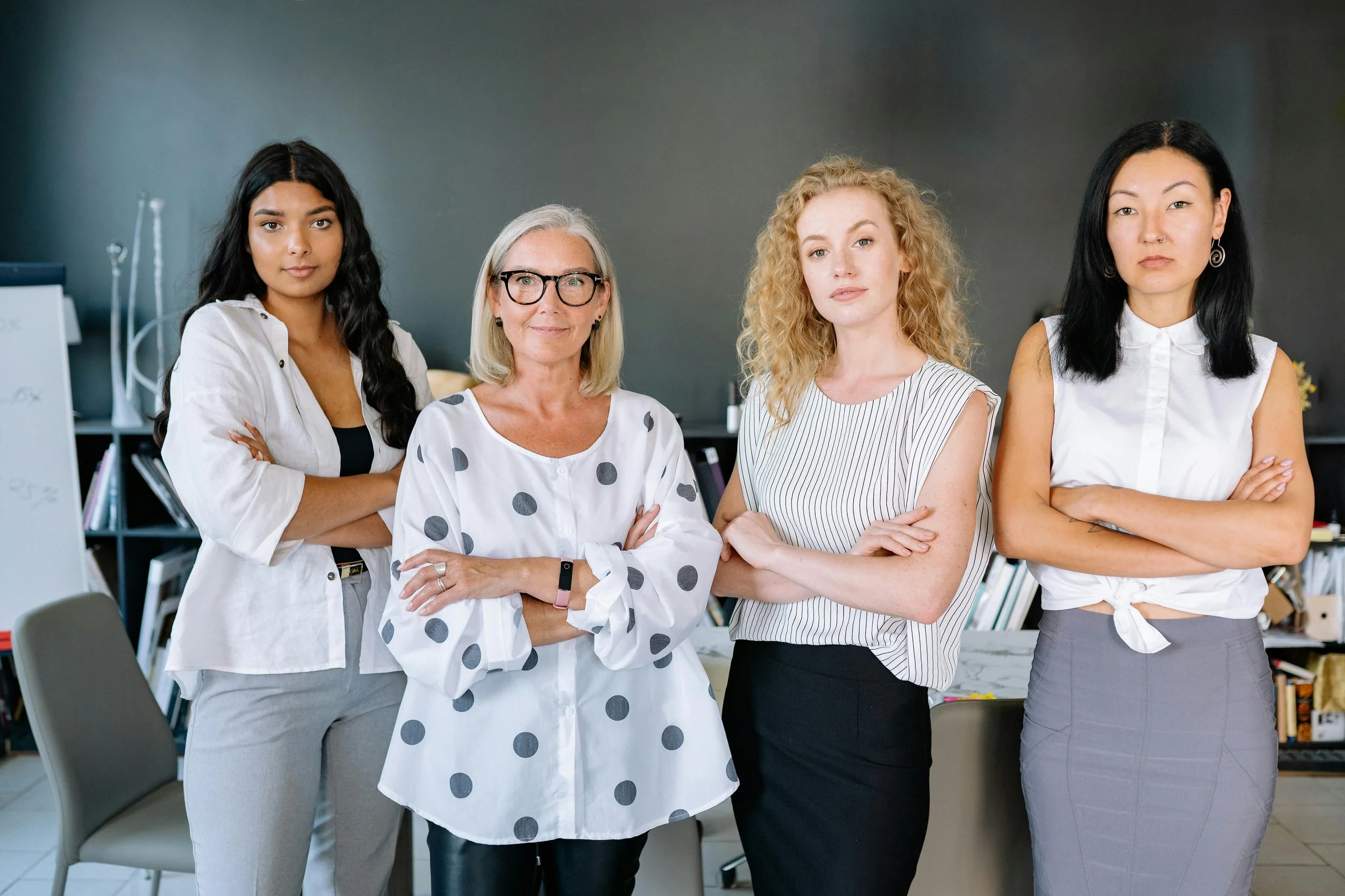 Four professional women standing confidently with arms crossed in an office setting, symbolizing leadership, structure, and outcome driven success planning.