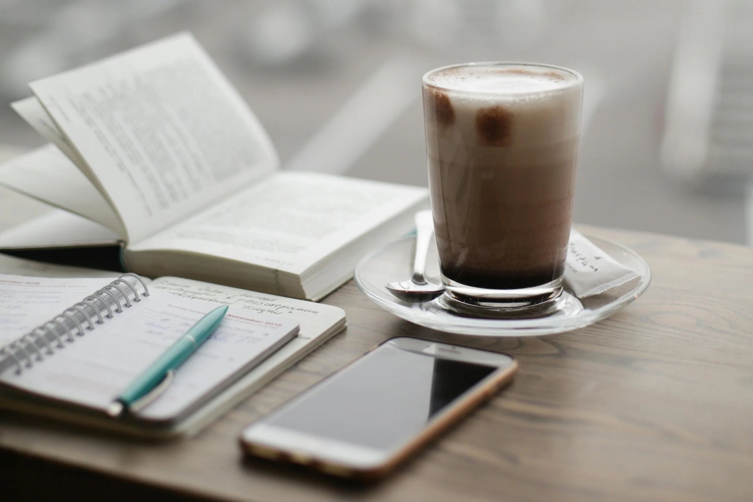 Minimal workspace with coffee, open notebook, and phone, representing a slow, focused approach to productivity and daily planning