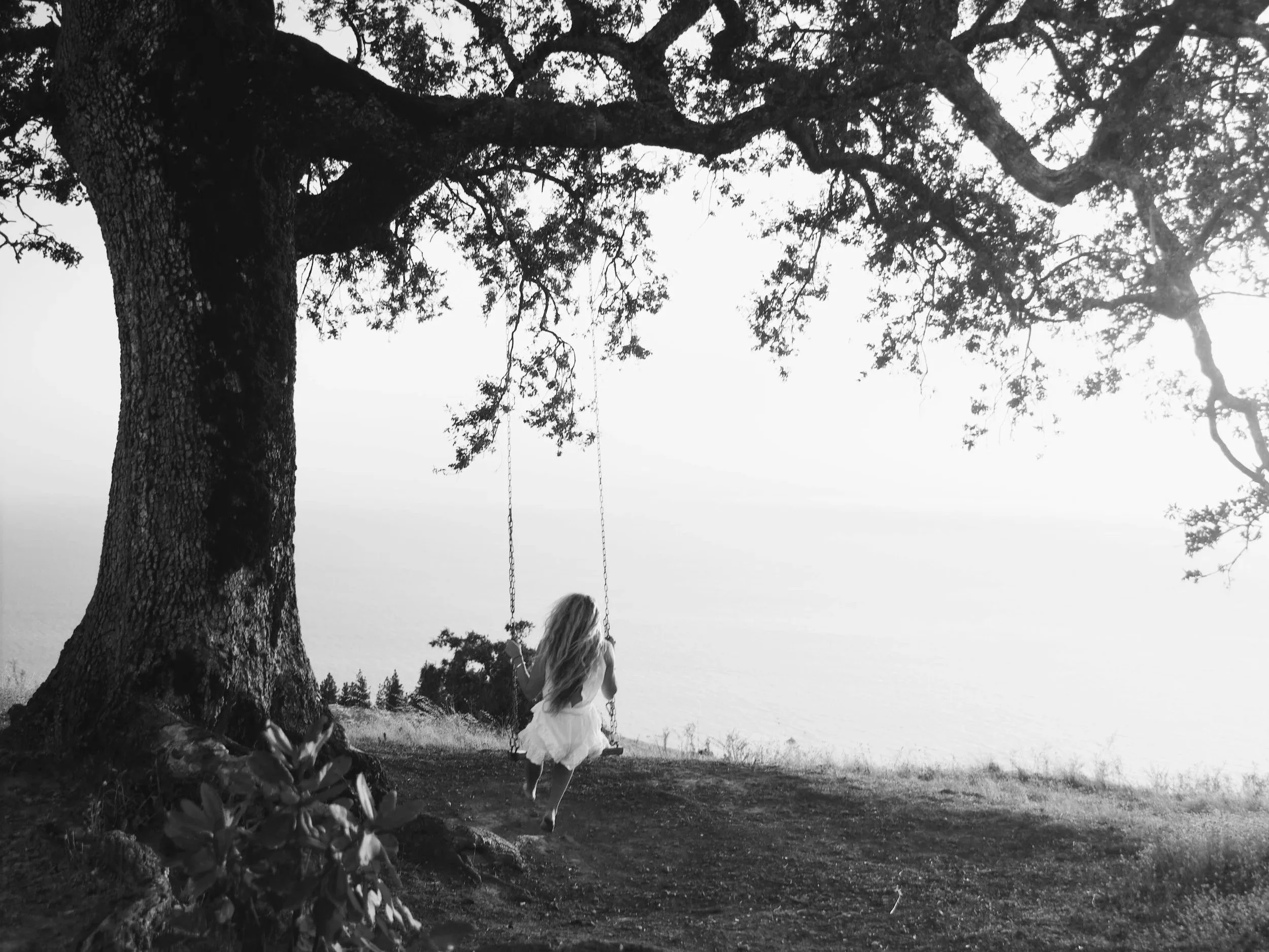 A woman sits quietly on a swing beneath a tree, relaxed and present, enjoying a calm moment of fulfillment.