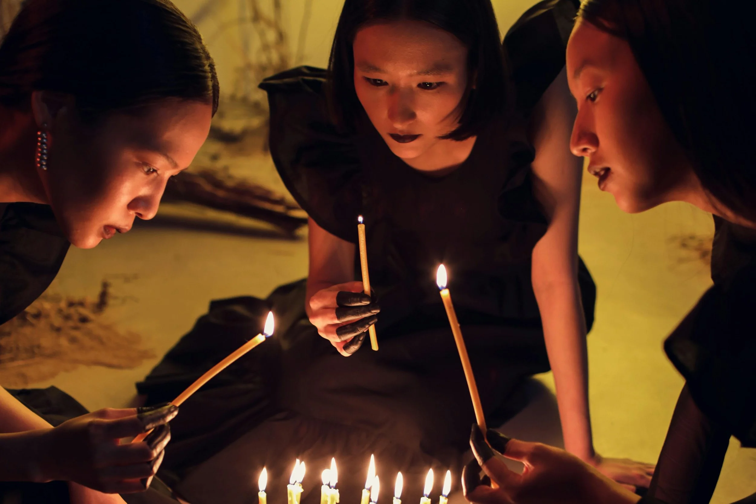Three women leaning over lit candles in a dimly lit room, representing intentional focus, strategic planning, and outcome driven vision.