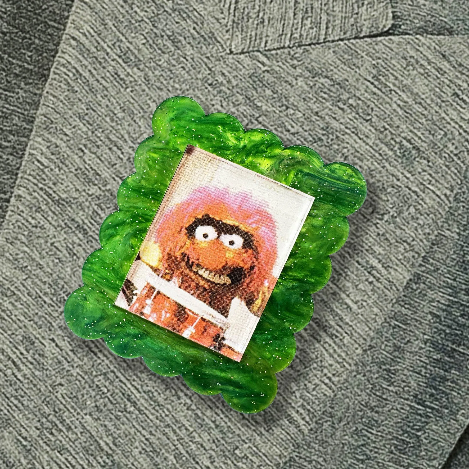A green glitter acrylic brooch featuring a picture of Animal from The Muppet Show