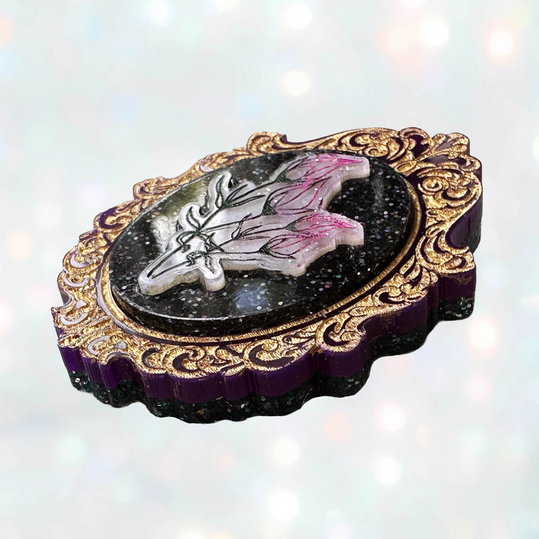 A laser cut acrylic cameo style brooch featuring a bunch of flowers within a purple and gold frame
