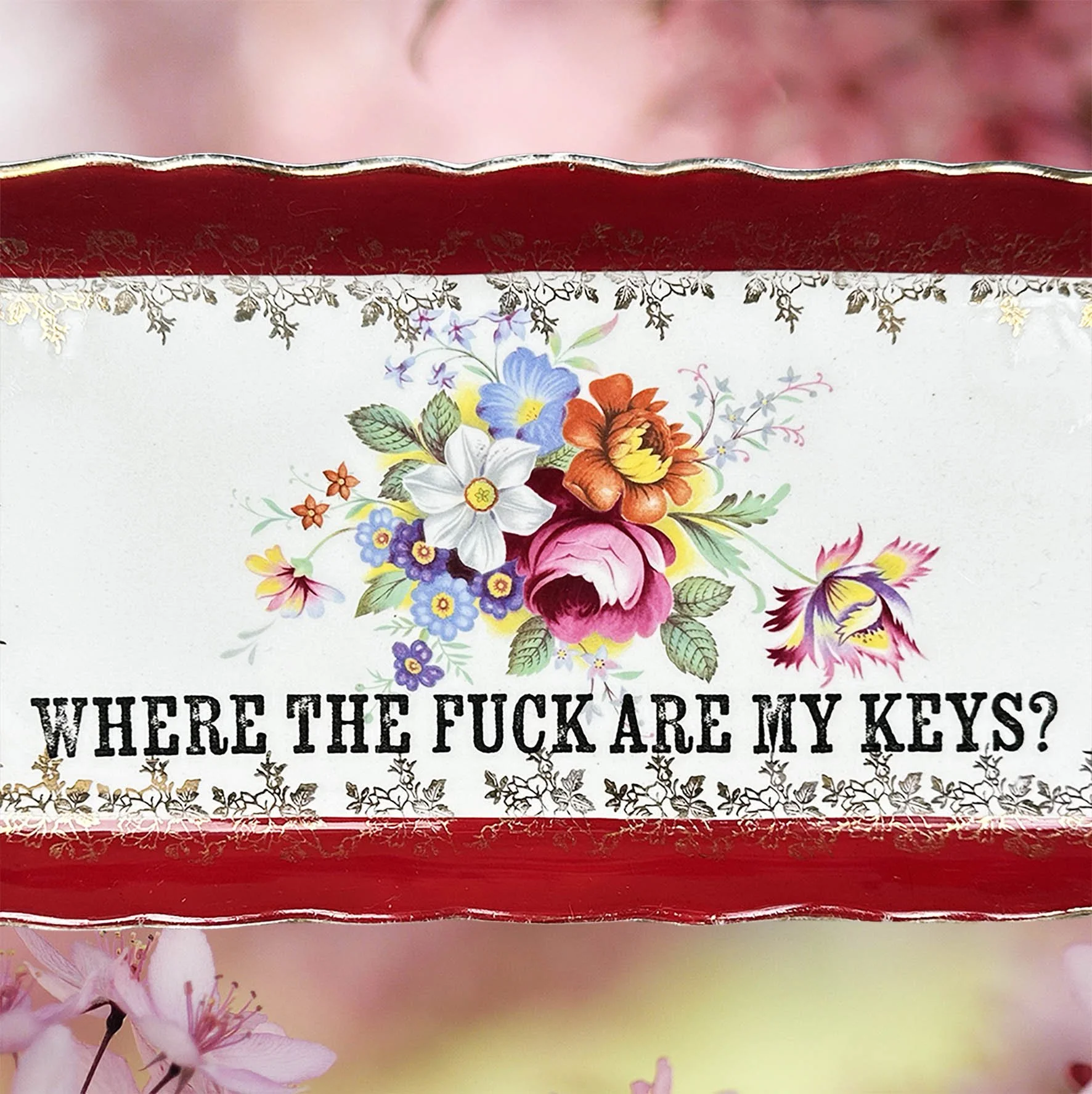 A vintage trinket dish with a red border and a floral design with the words “where the fuck are my keys?”