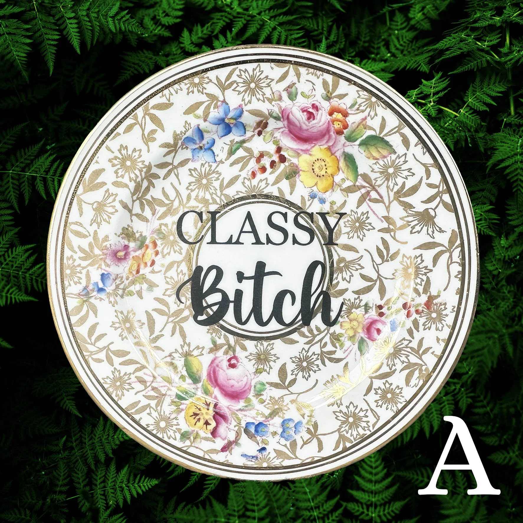 A vintage plate with a gold and pink floral design and the words "classy bitch" in black writing