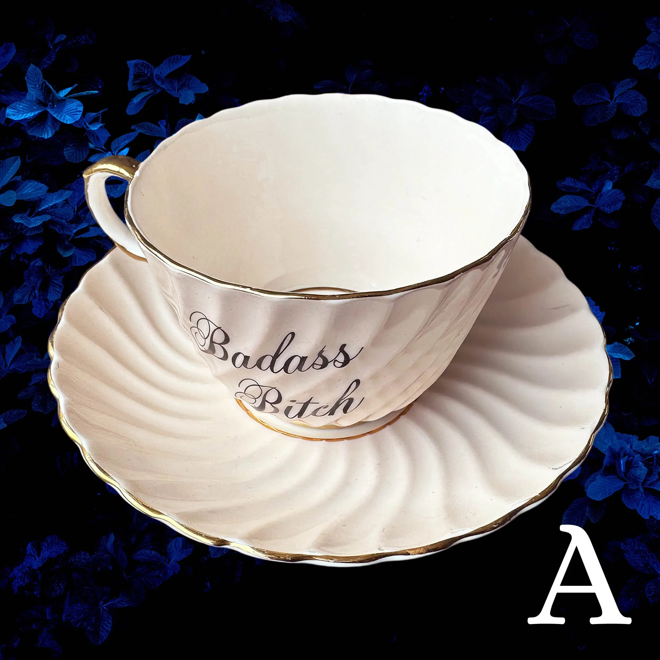 A soft pink vintage tea cup and saucer set with the words "badass bitch" in black cursive writing