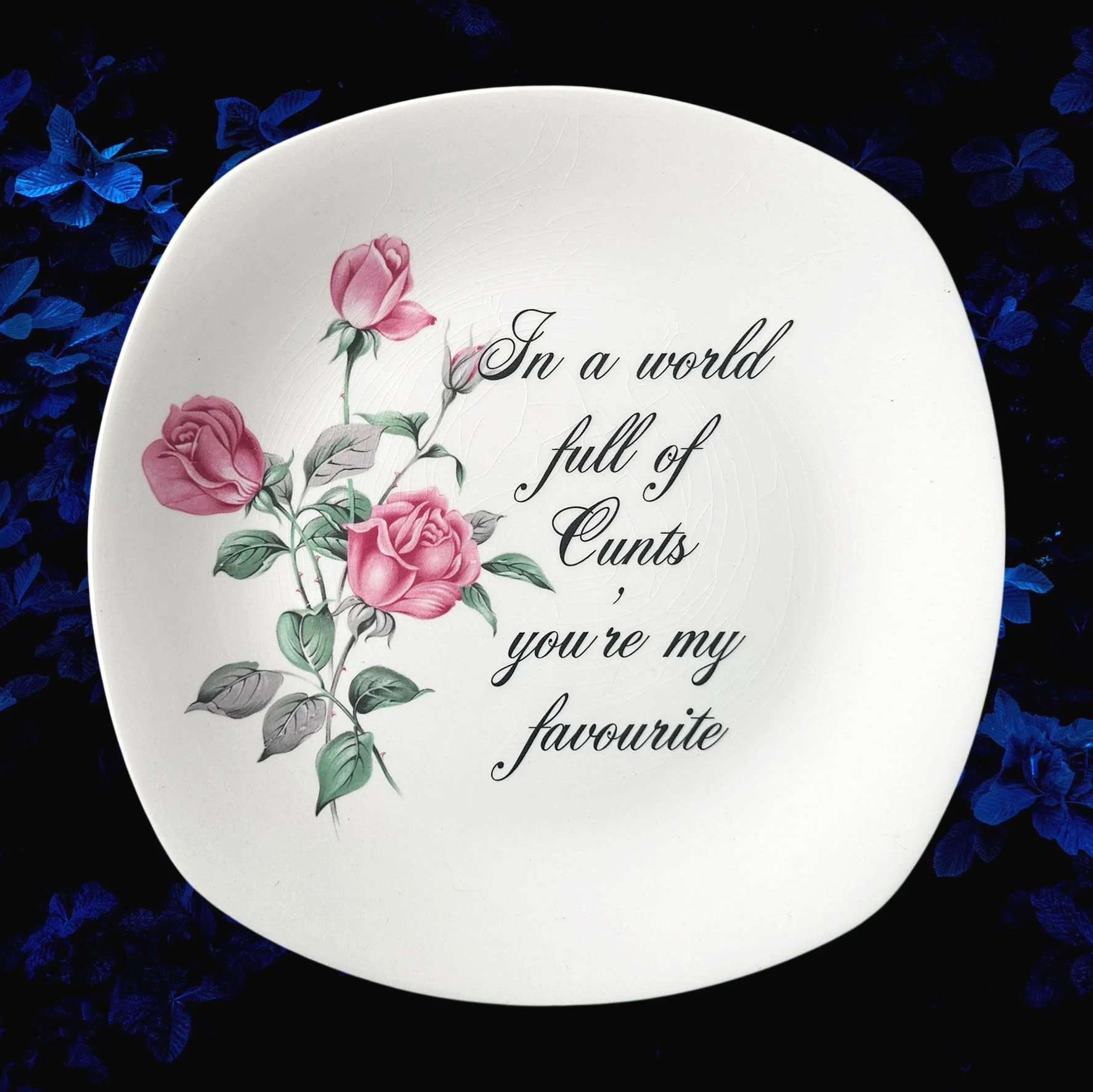 A vintage plate with pink roses and the words "In a world full of cunts you're my favourite"