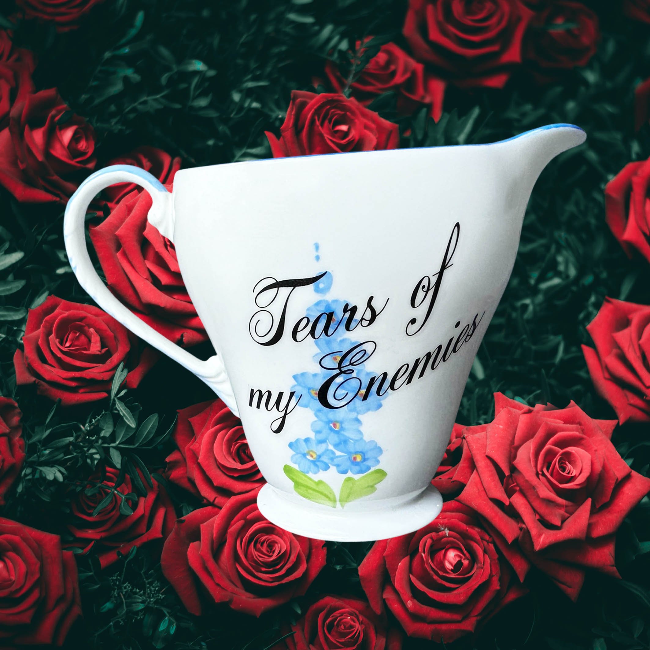 A vintage milk jug with blue flowers, the words “tears of my enemies” in black cursive writing