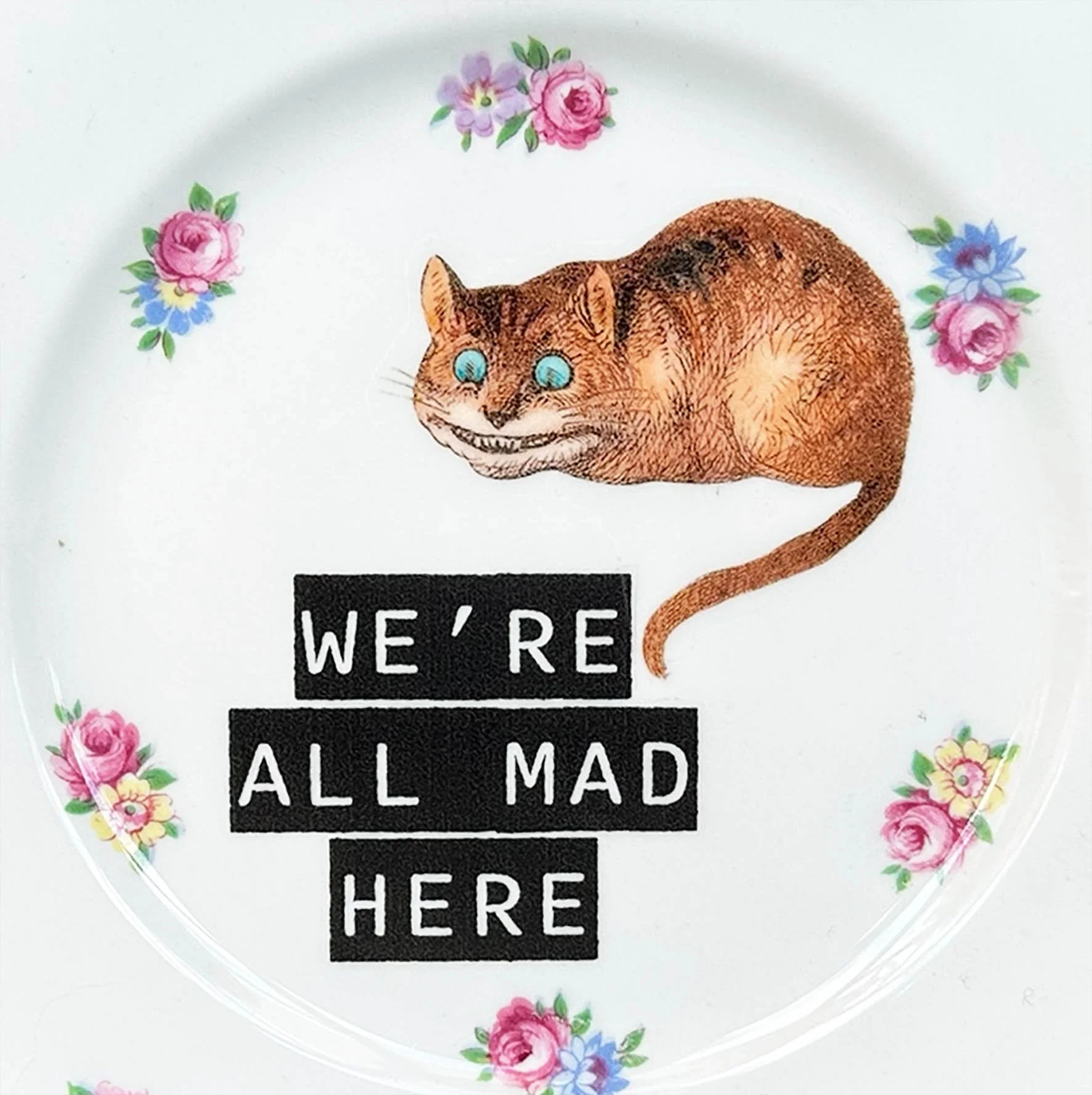 A vintage plate with a picture of the Cheshire Cat and the quote “we’re all made here”