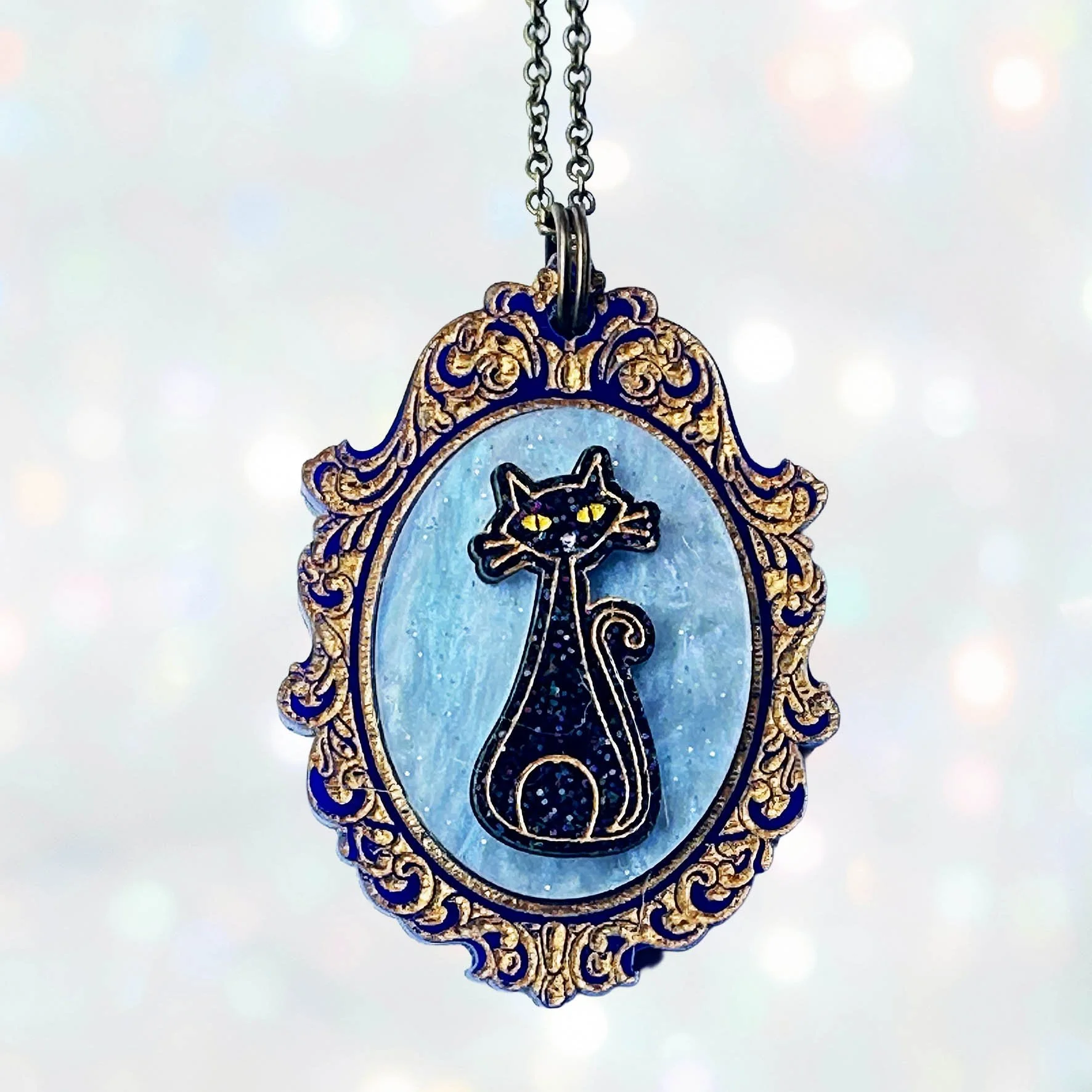 A laser cut acrylic cameo style necklace featuring a black cat inside inside a gold frame