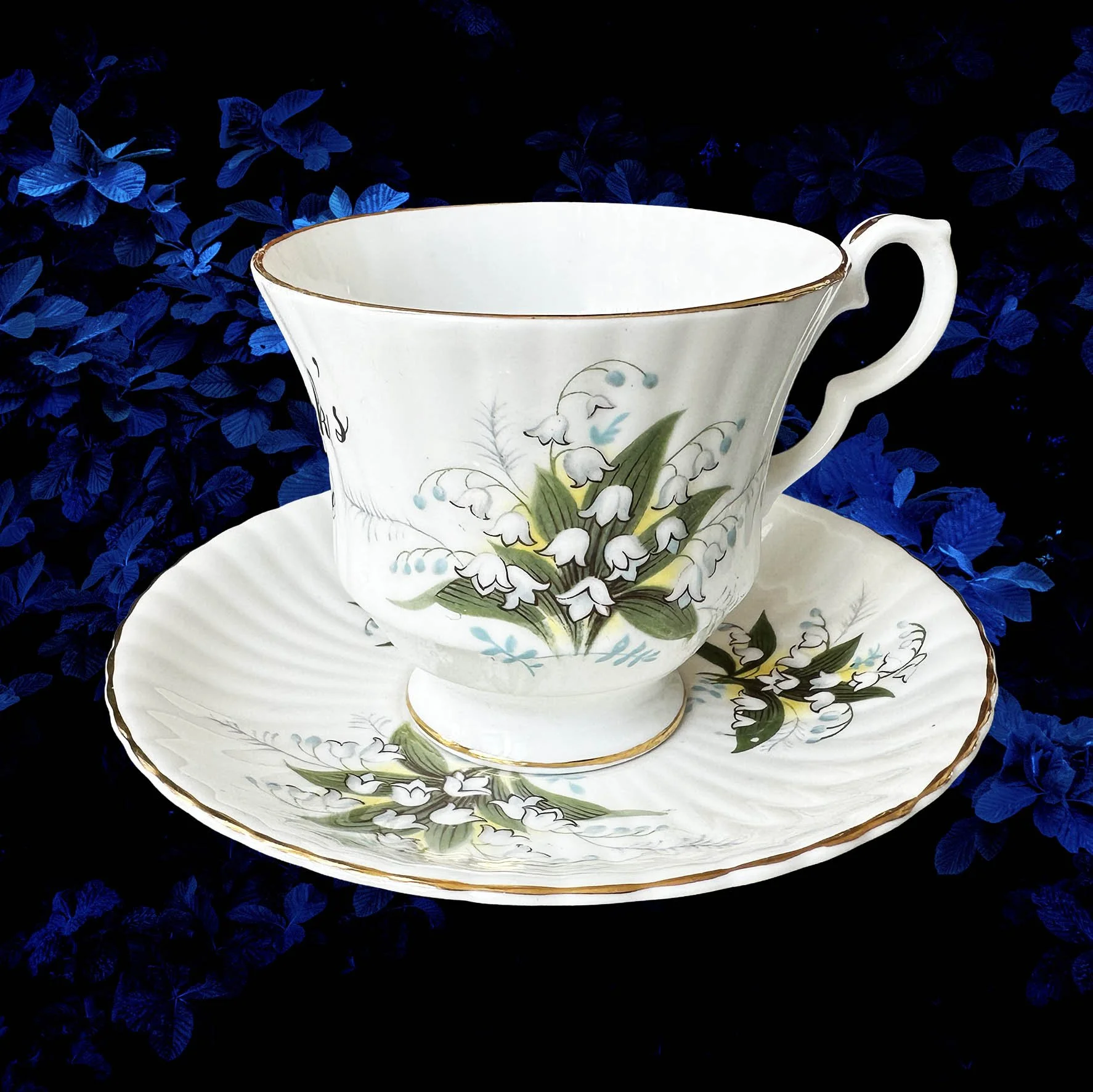 A vintage tea cup with a white and green floral design and a quote “for fuck’s sake” in black writing