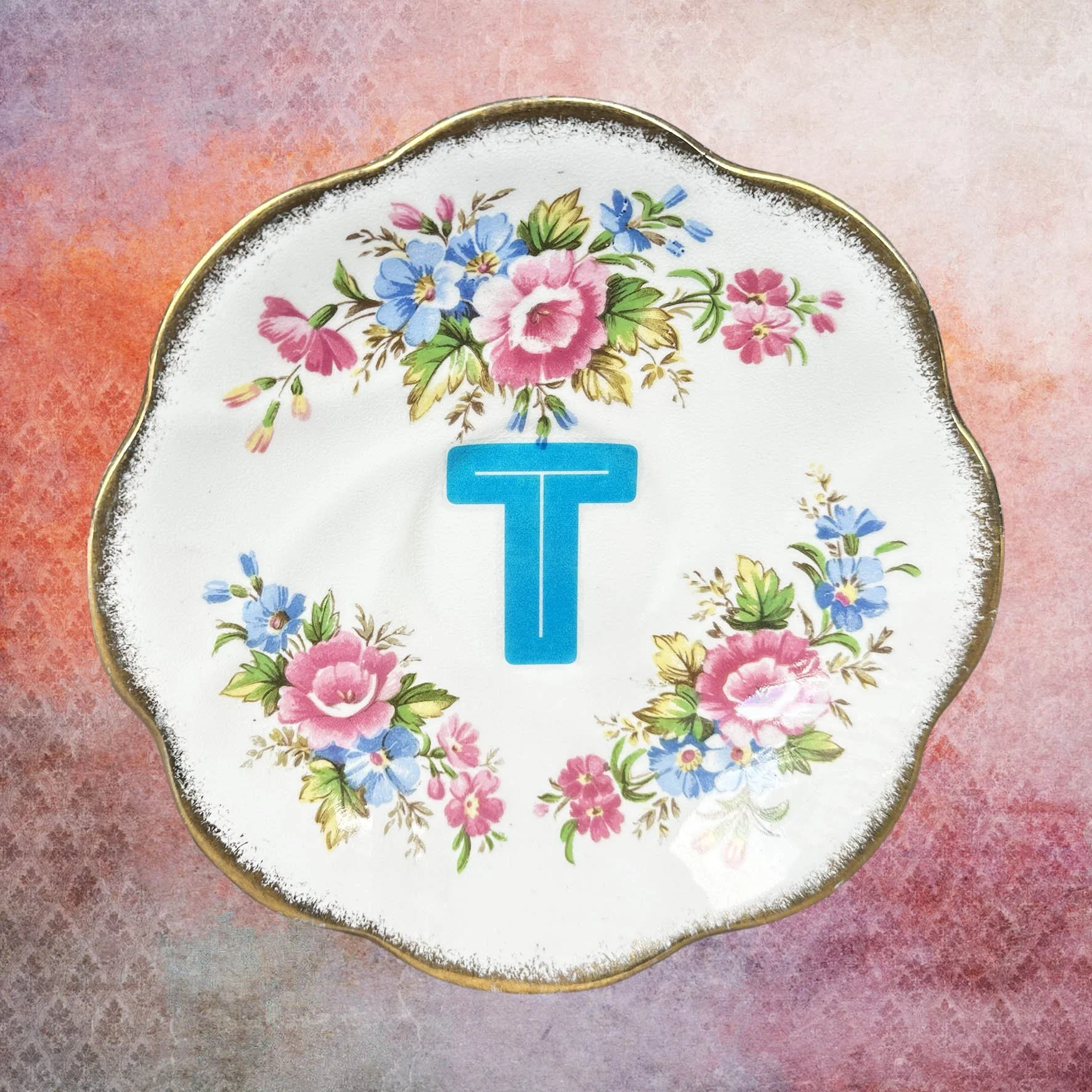 A vintage saucer with pink flowers and a blue letter “t”