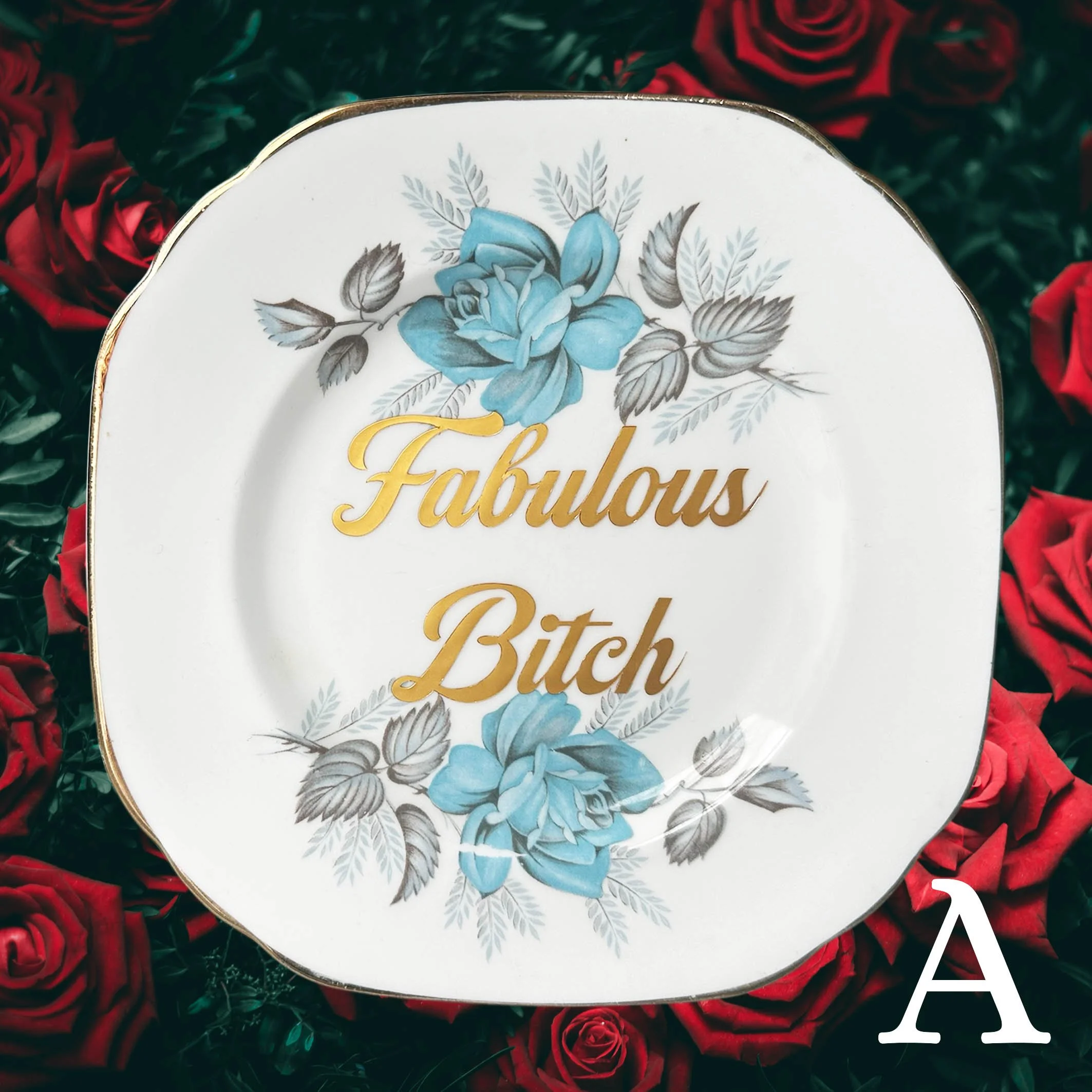 A vintage decorative wall plate with a blue floral design and the words “fabulous bitch” in gold lettering