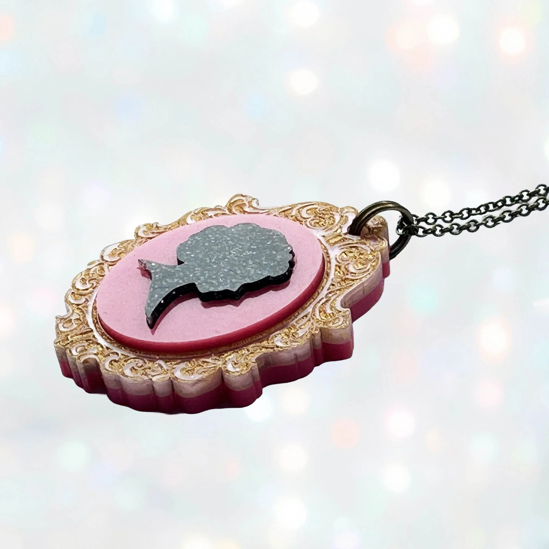 A pink, gold and black glitter laser cut acrylic cameo style necklace featuring a silhouette