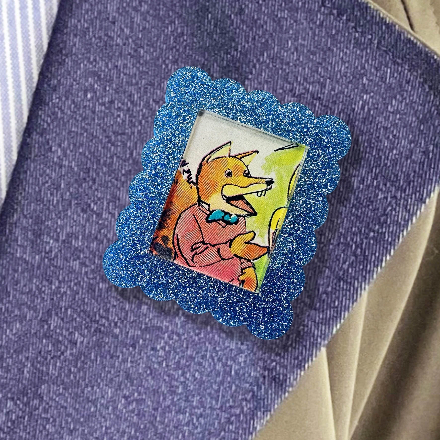 A light blue glitter acrylic brooch featuring a picture of Basil Brush