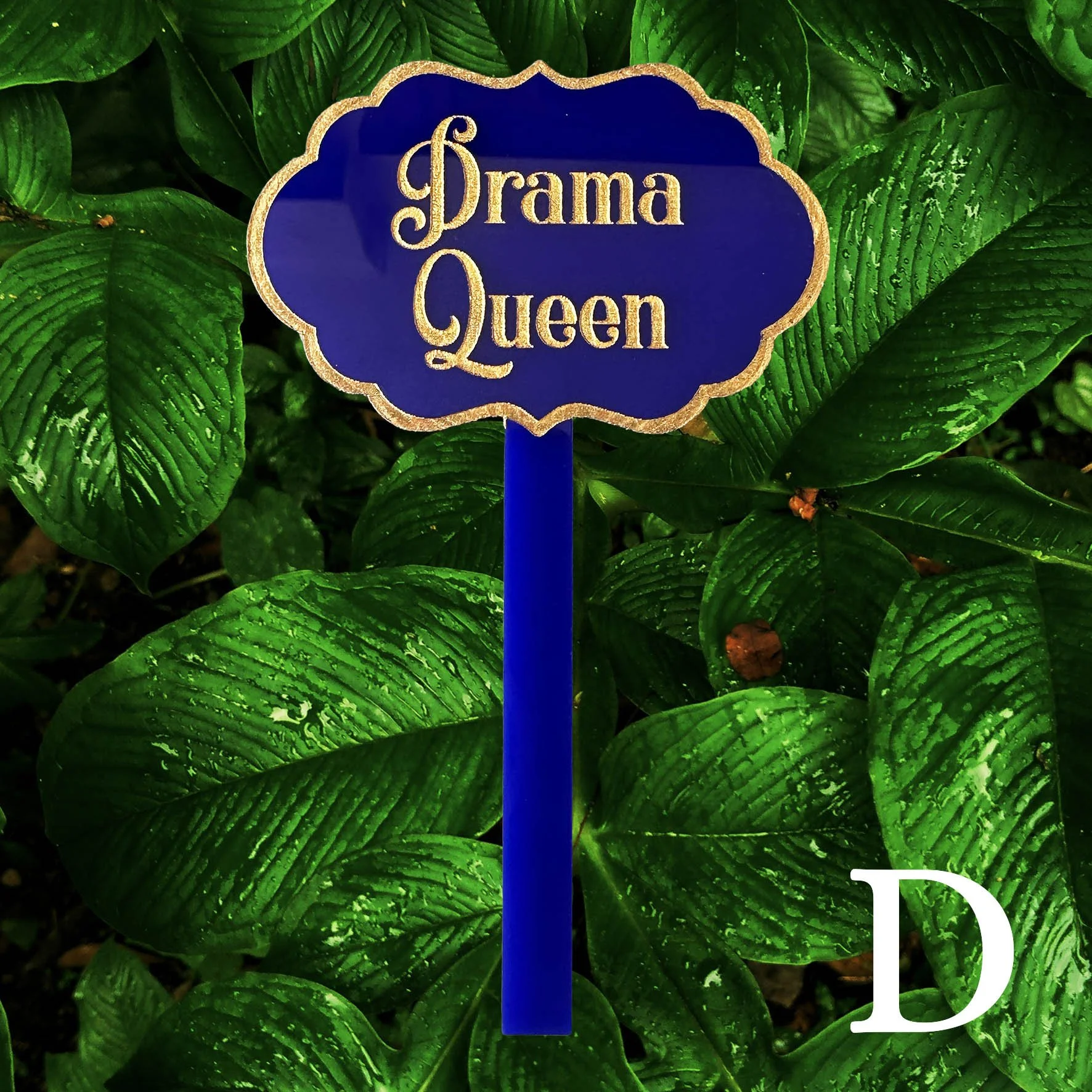 D, Blue acrylic planter stick label with the words "drama queen" in gold lettering