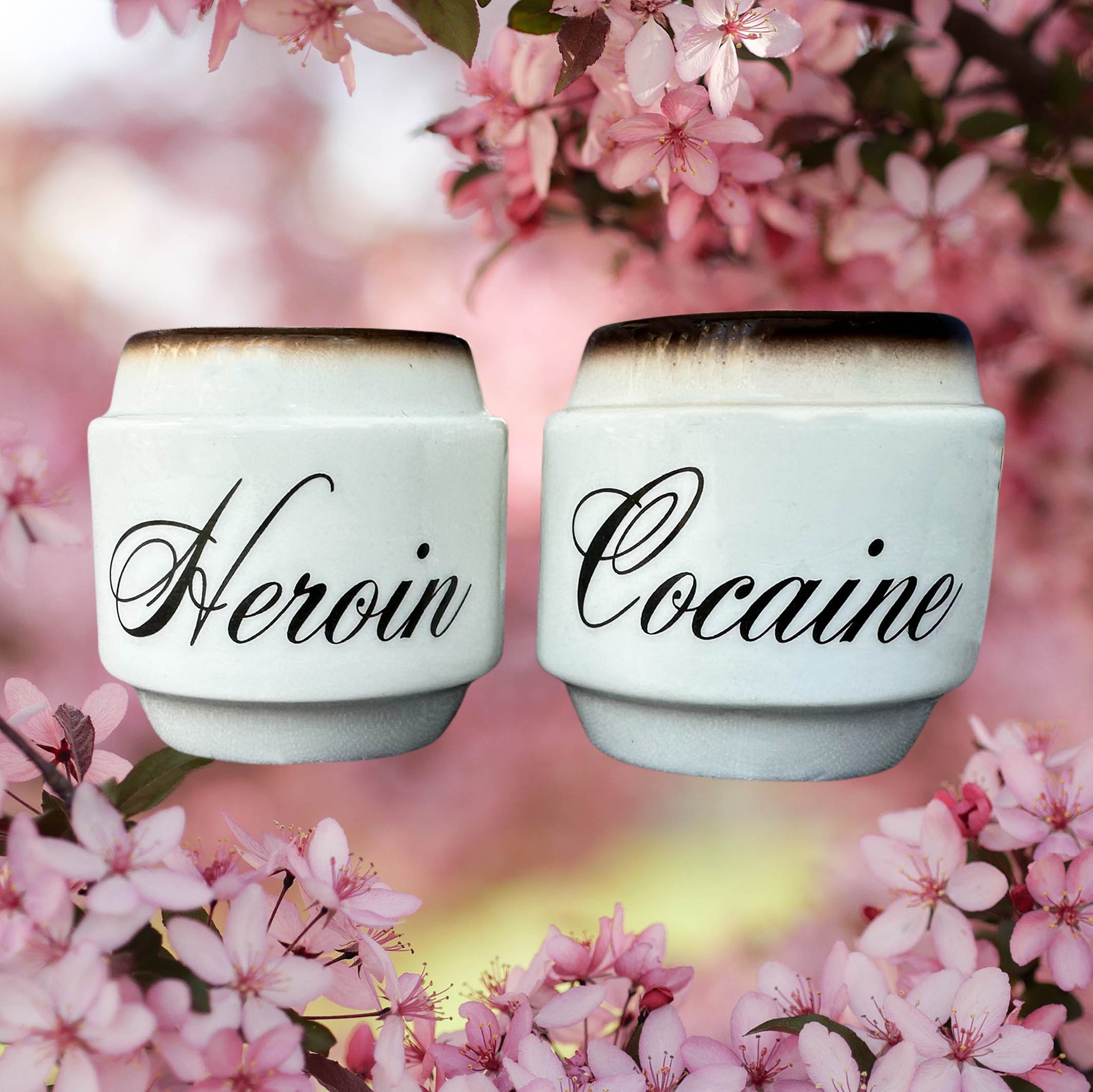 Cream coloured salt and pepper shakers with brown detailing, the words “heroin” and “cocaine” in black cursive writing