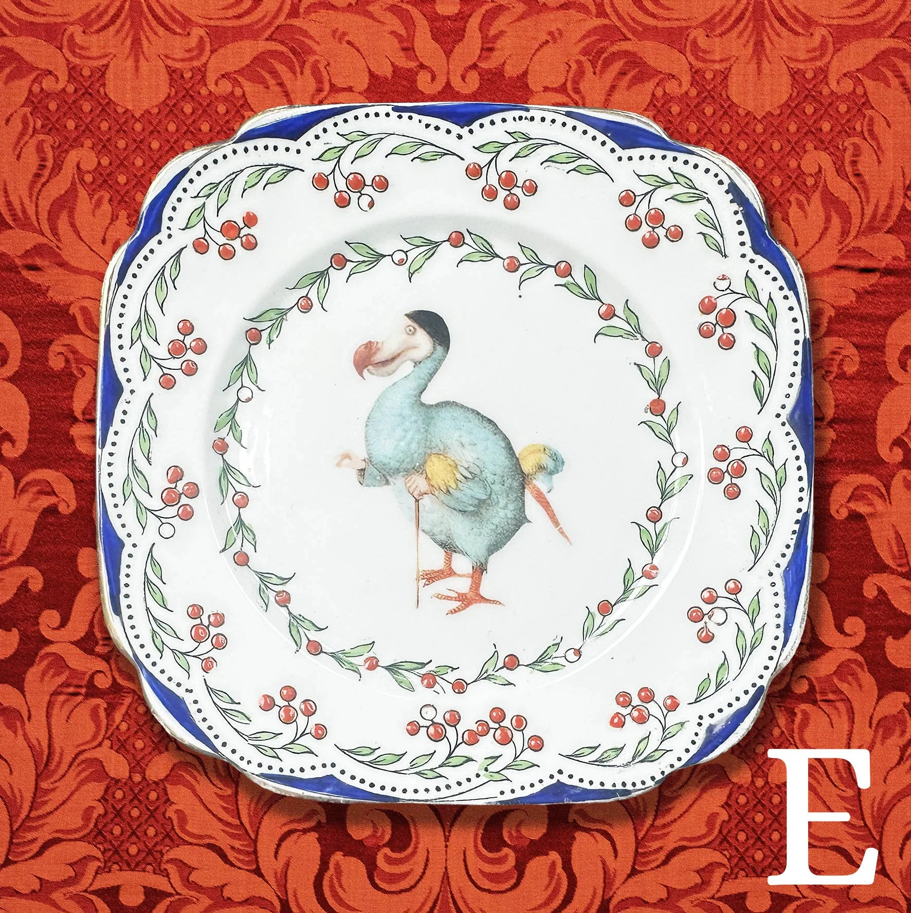 Saucer E: a small plate with a blue and red floral design and a picture of the Dodo from Alice in Wonderland