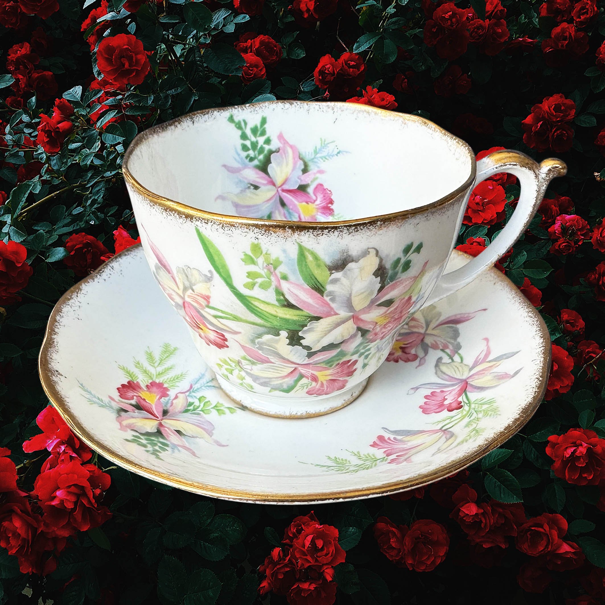 A vintage tea cup and saucer set with a pink floral design and the word "Whore" in black cursive writing