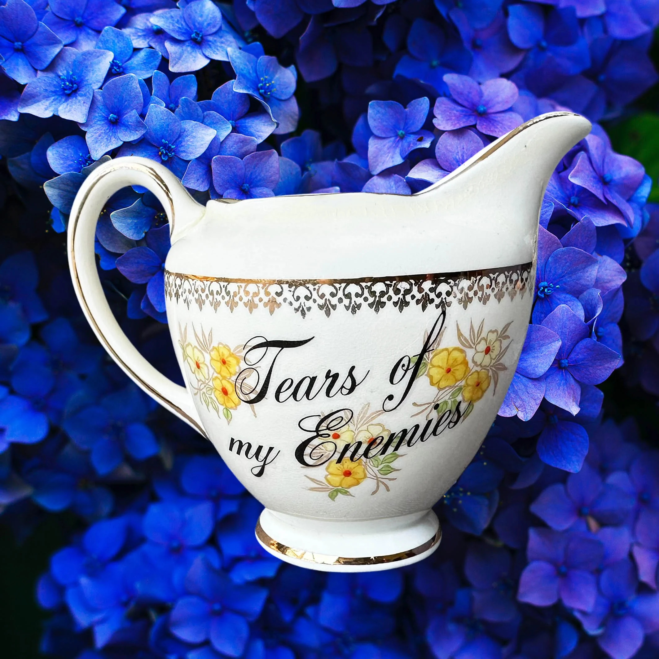 A cream vintage milk jug with yellow flowers, the words “tears of my enemies” in black cursive writing